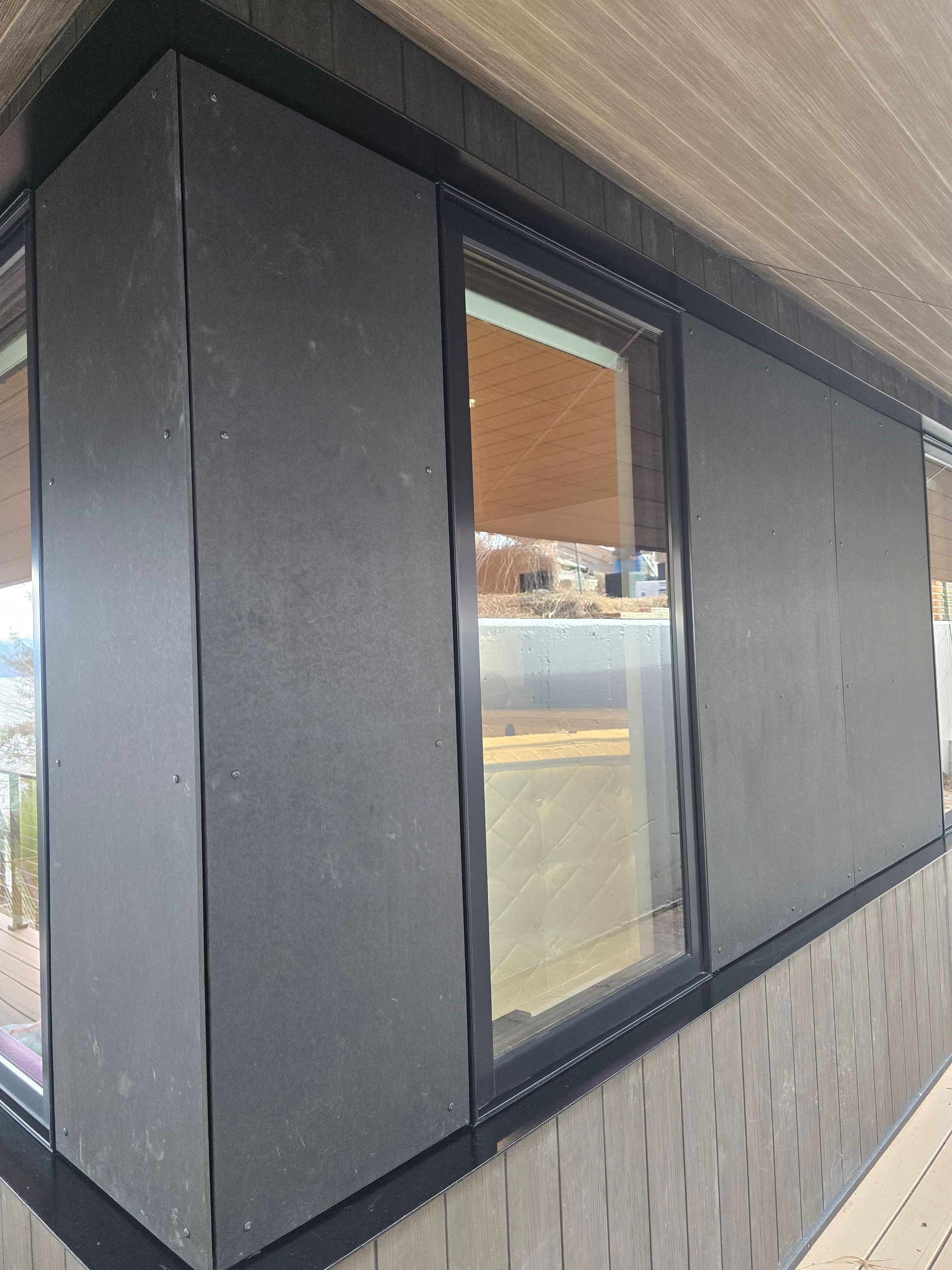An exterior view of a building corner showing matte black wall panels installed around a window.