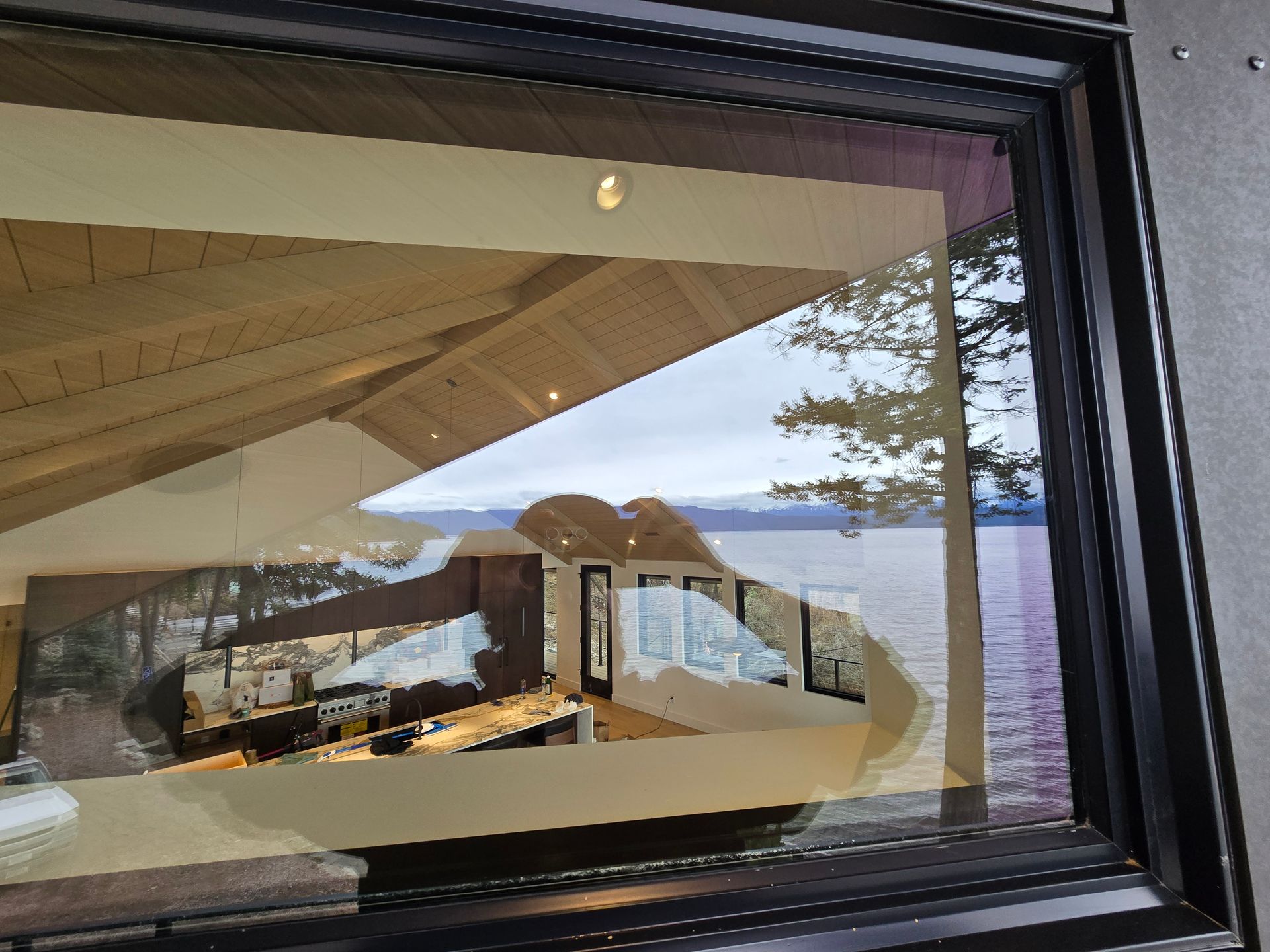 Reflective window showing an indoor restaurant area with tables, looking out onto a lake and trees under a cloudy sky.