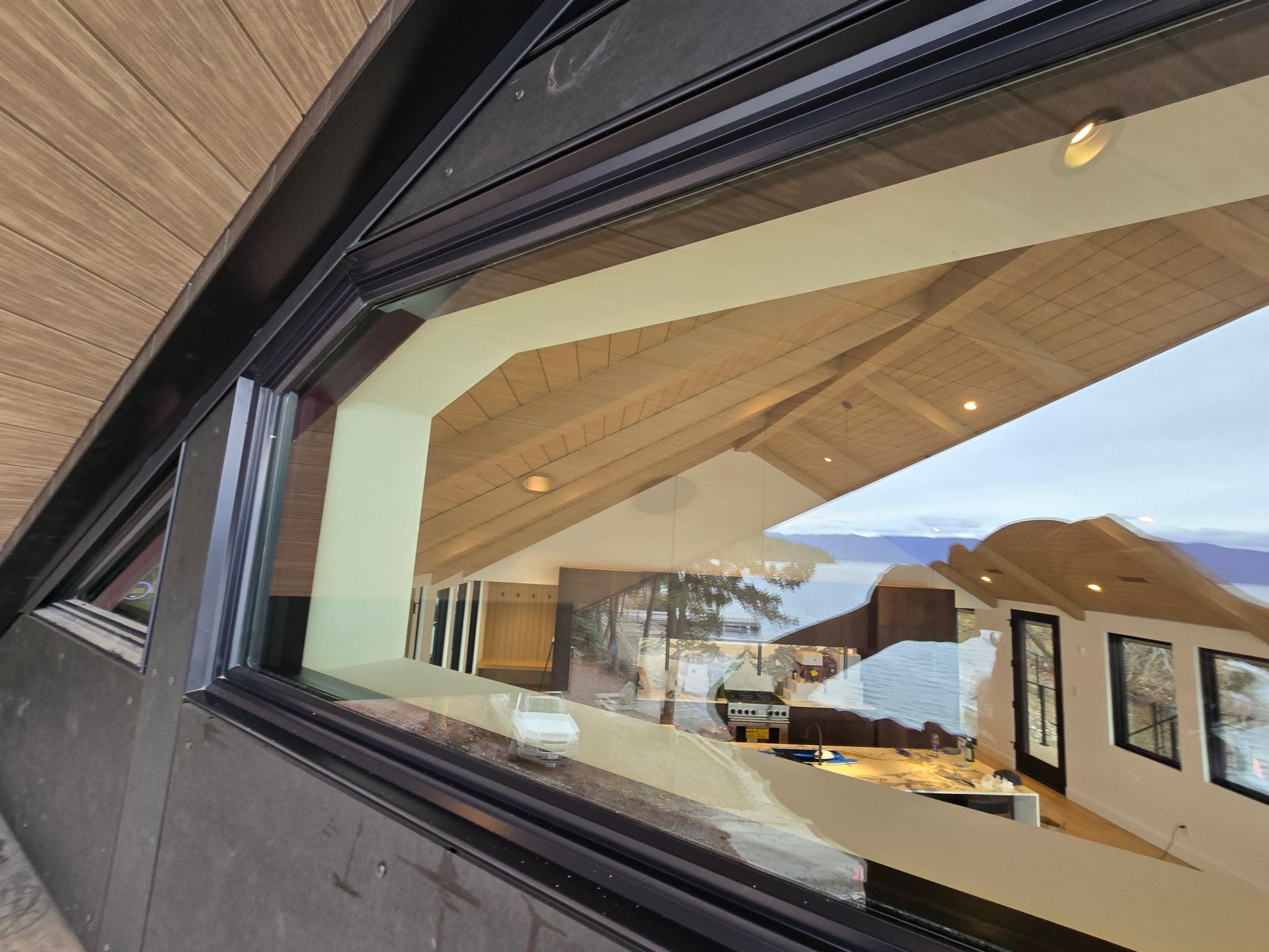 A low-angle view looking through a black-framed window into a modern, light-filled interior with vaulted wood ceilings.