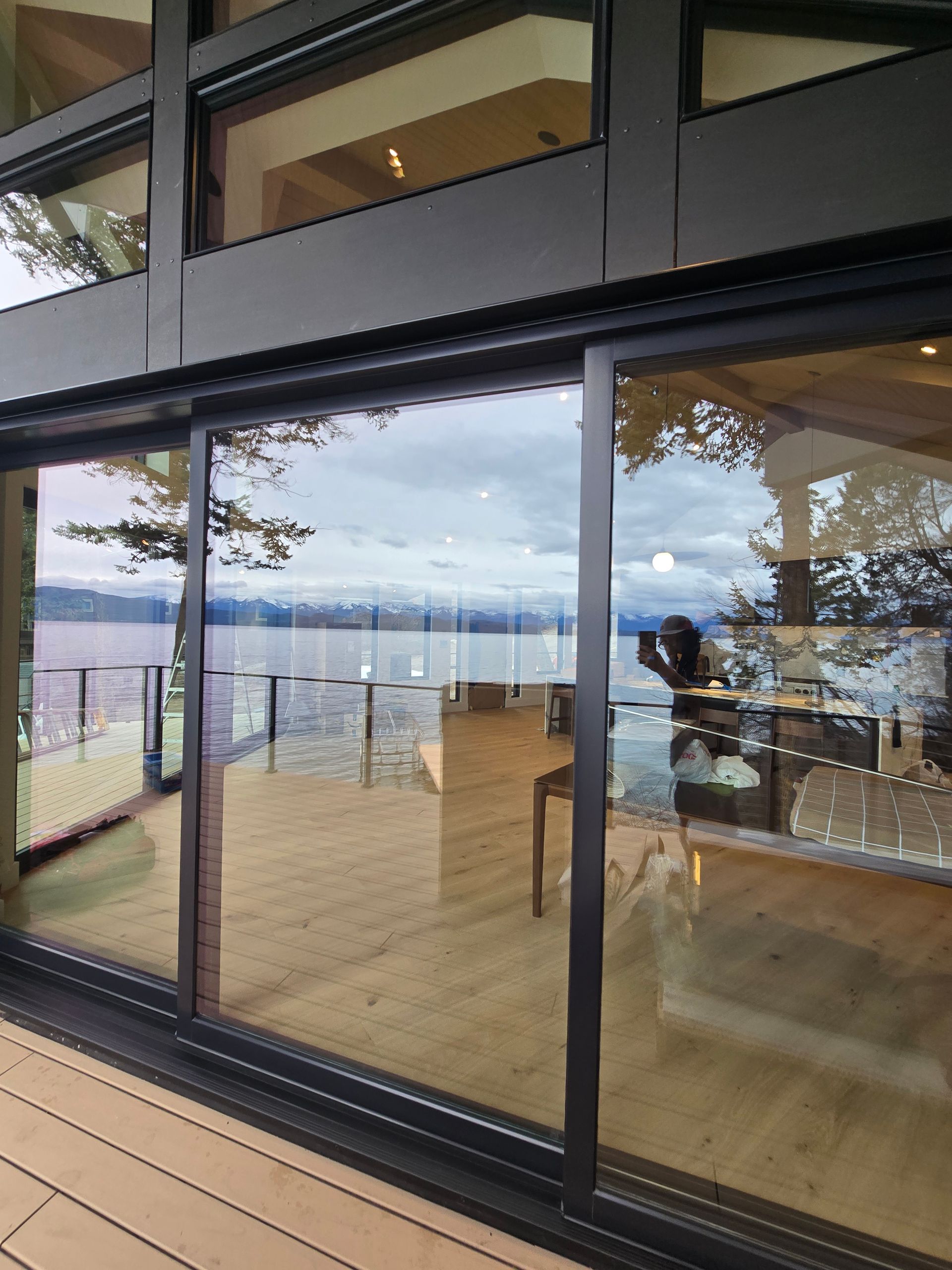 Sliding glass doors open to a deck overlooking a wide body of water and distant hills under a cloudy sky.