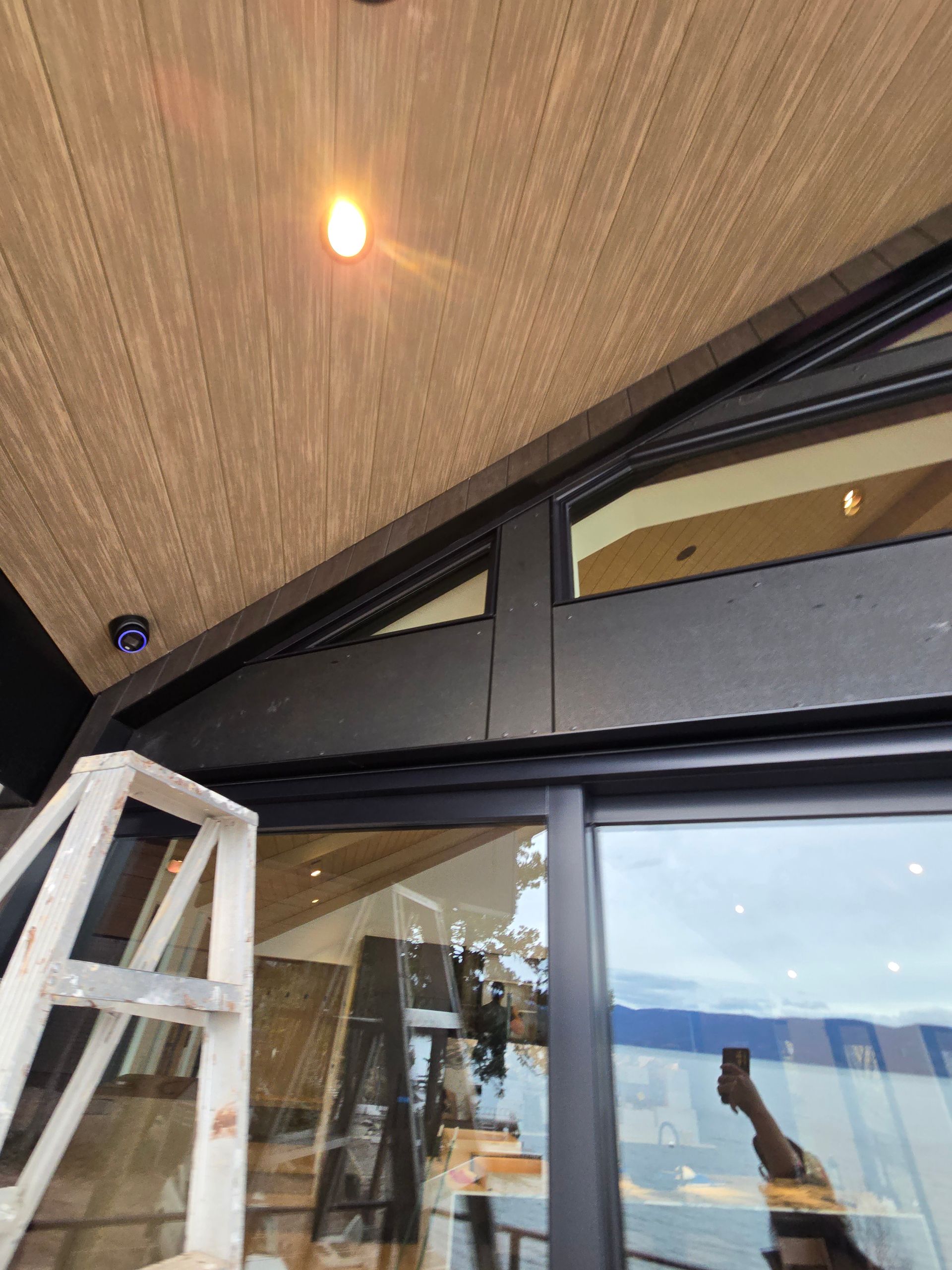 A white step ladder positioned in front of a modern dark-framed window under a wooden ceiling.