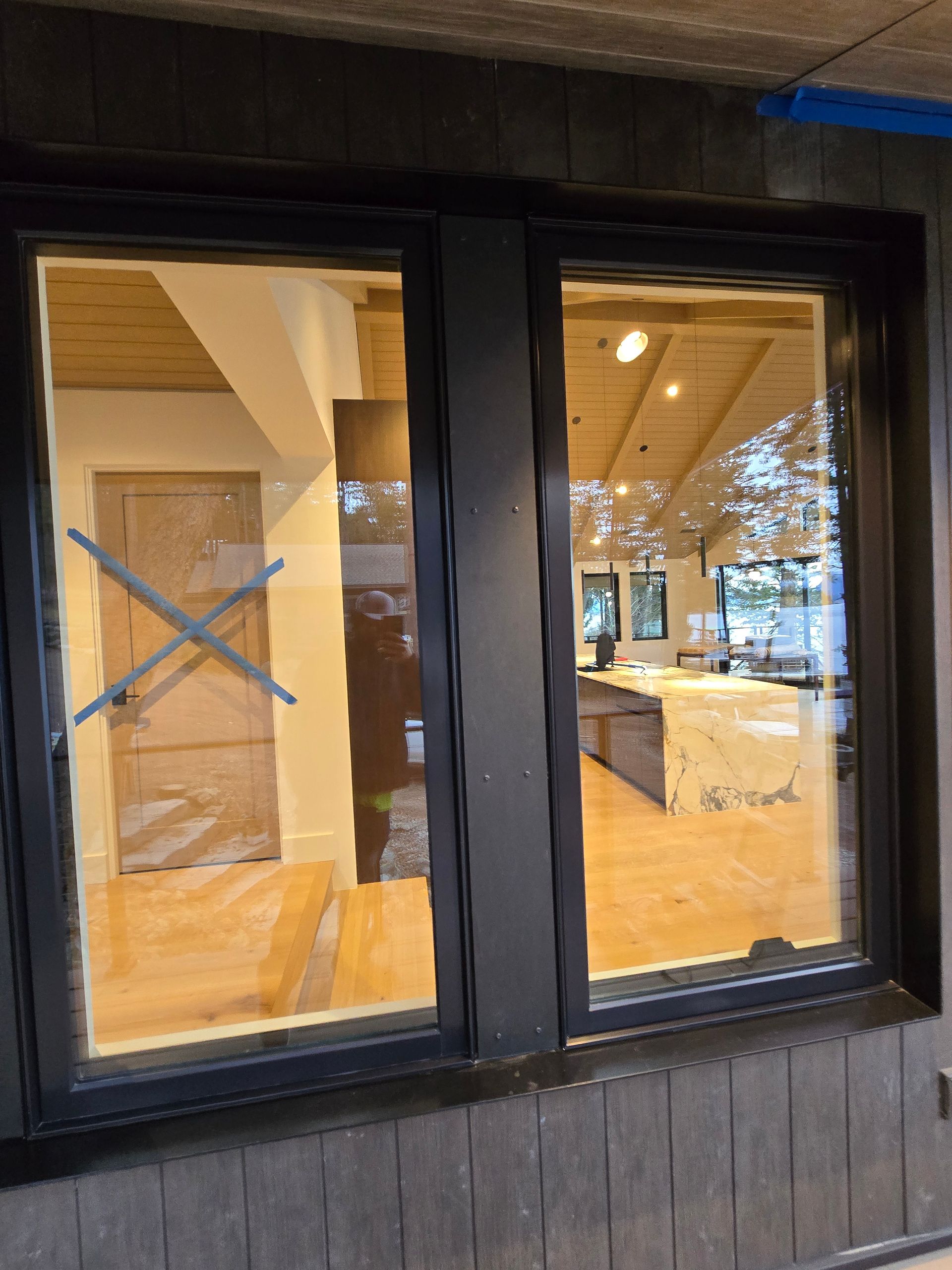 A double window with black frames installed on a dark exterior wall, looking into a bright, modern interior room.