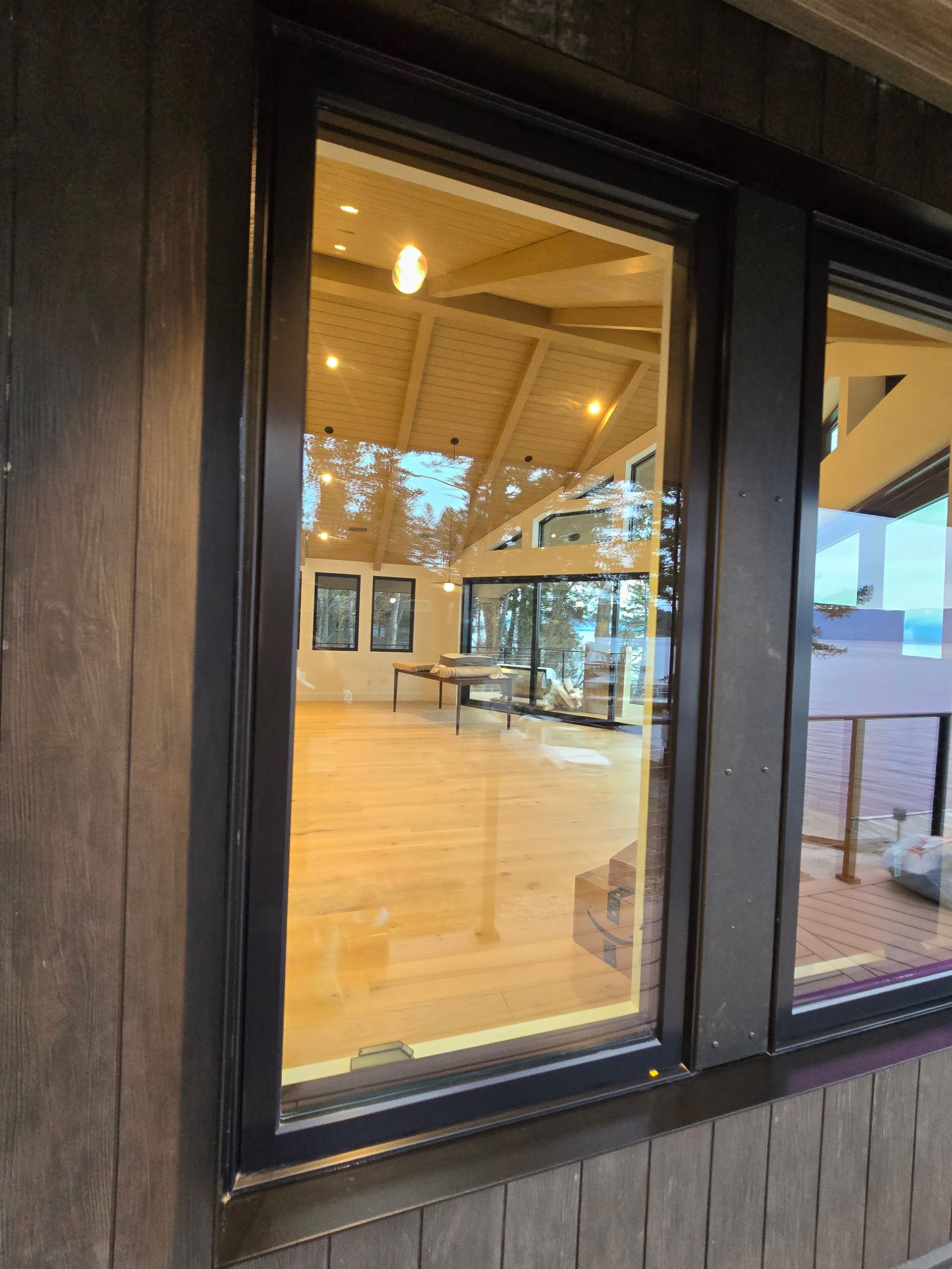 A view looking through a dark-framed window into a bright, spacious room with vaulted ceilings and light wood floors.
