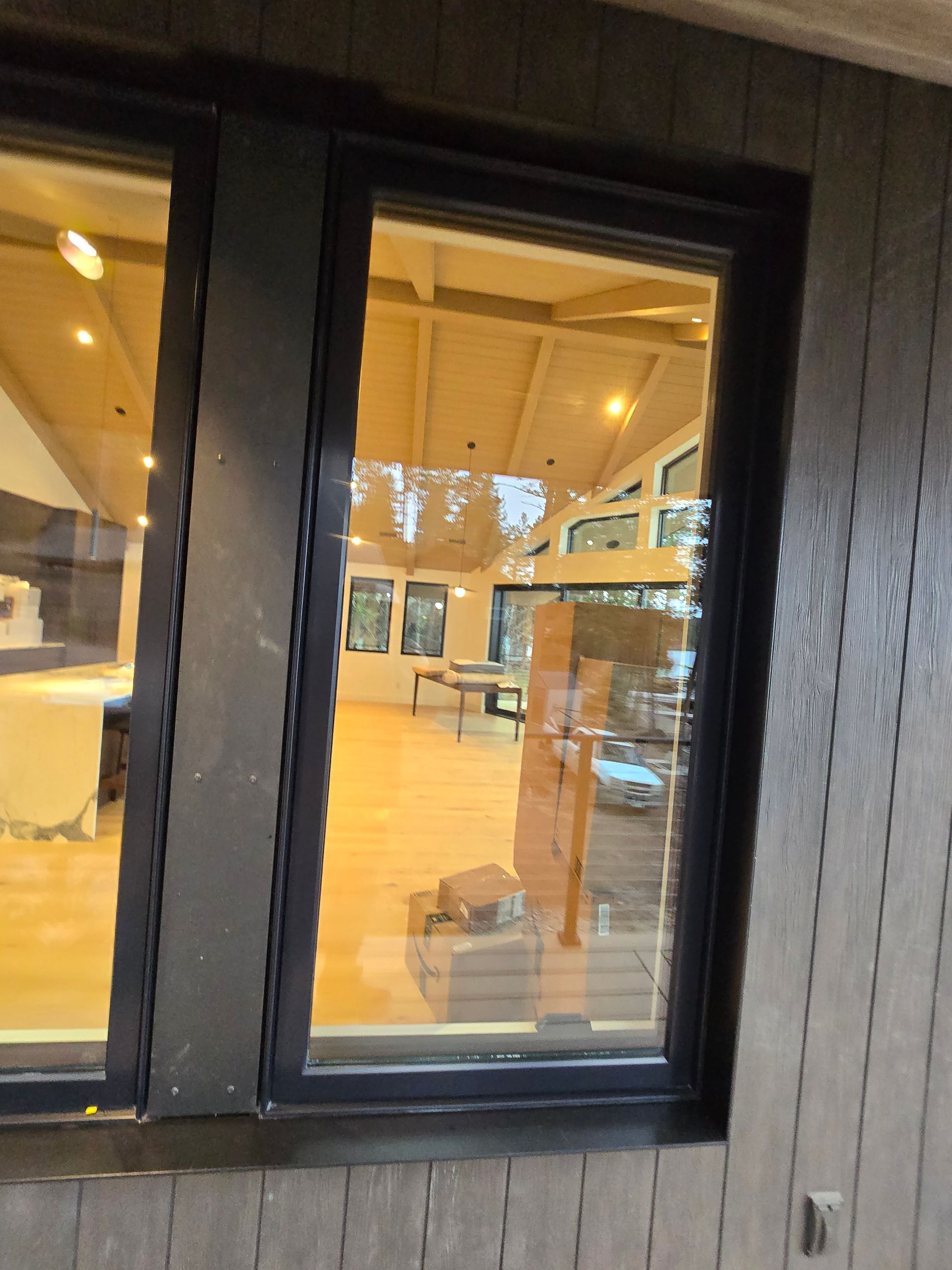 View through a dark-framed window showing an interior room with a sloped wooden ceiling and light-colored flooring.