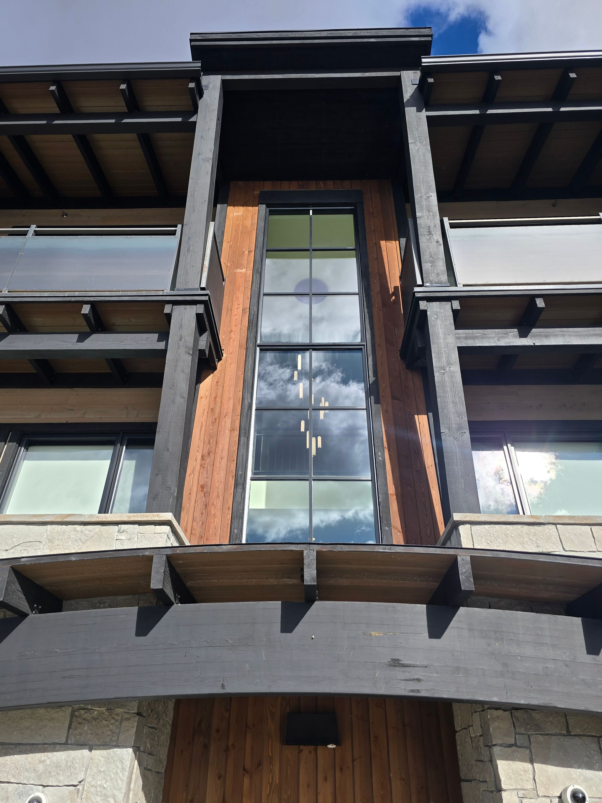 Modern home facade with black timber beams, stone accents, and a central vertical window reflecting the sky.