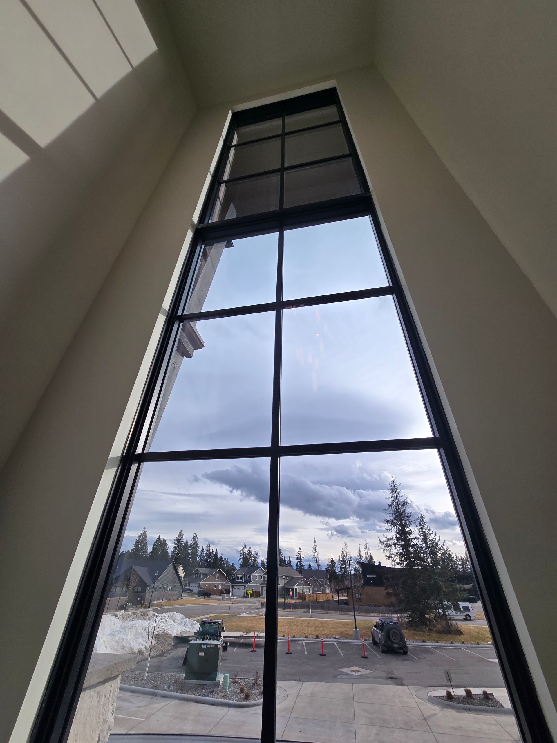 A tall, multi-pane window with black frames looking out over a neighborhood street with buildings and a cloudy sky.
