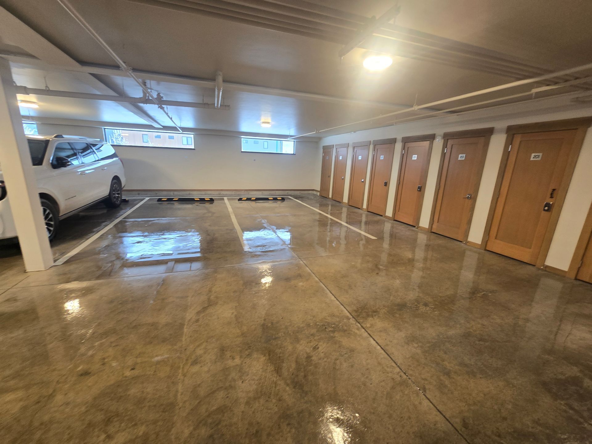 Indoor parking garage with a white SUV parked, polished concrete floors, and a row of wooden storage unit doors.
