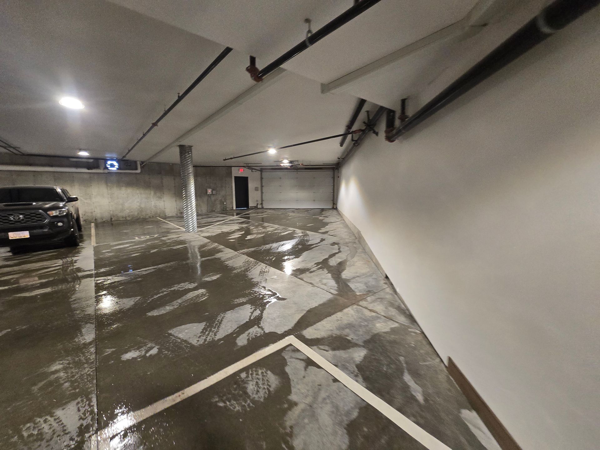 A wet parking garage with a parked black truck on the left and a painted white corner line on the floor.