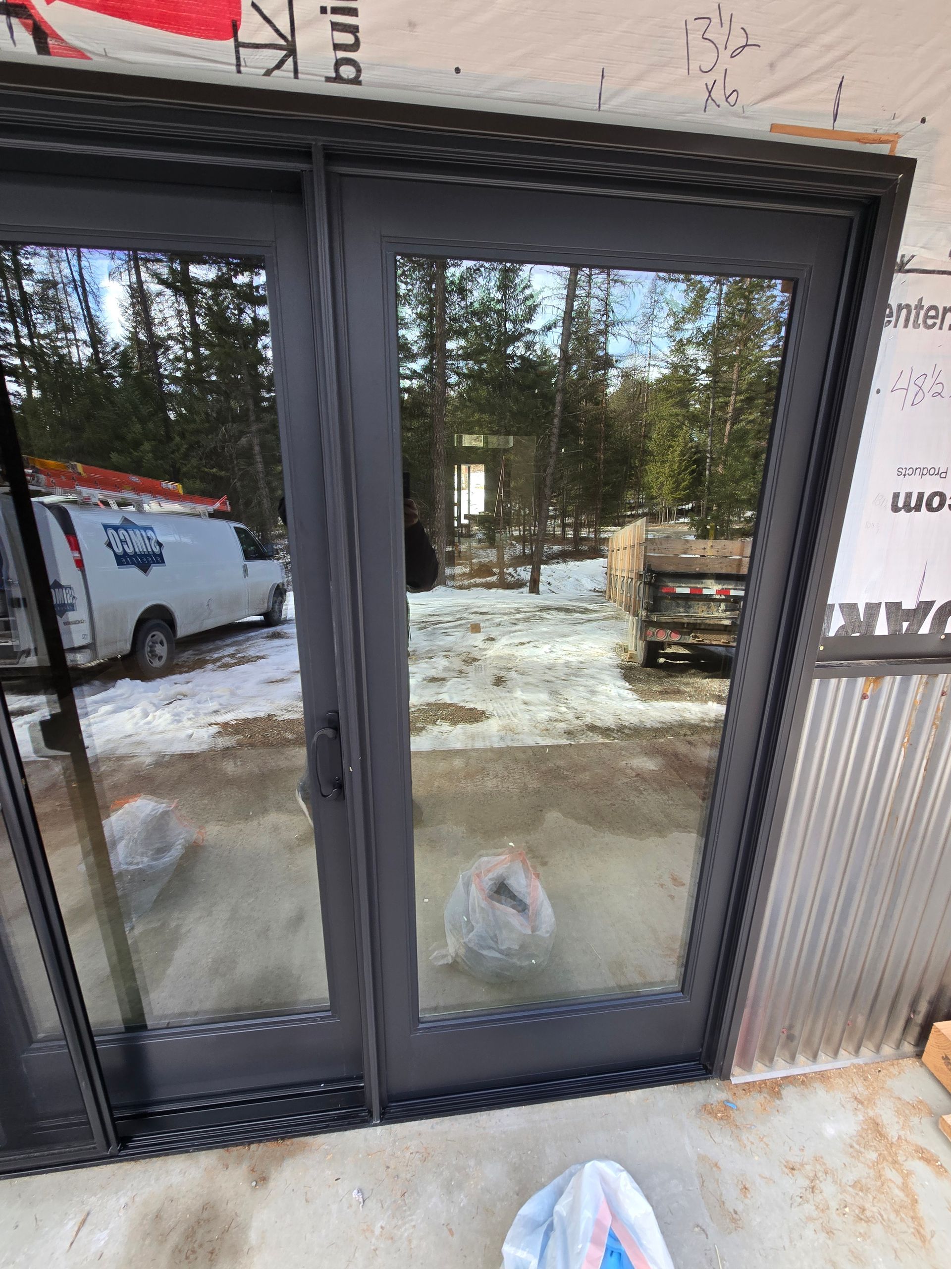 Dark-framed double glass doors installed in a structure under construction, viewed from an outdoor concrete patio.
