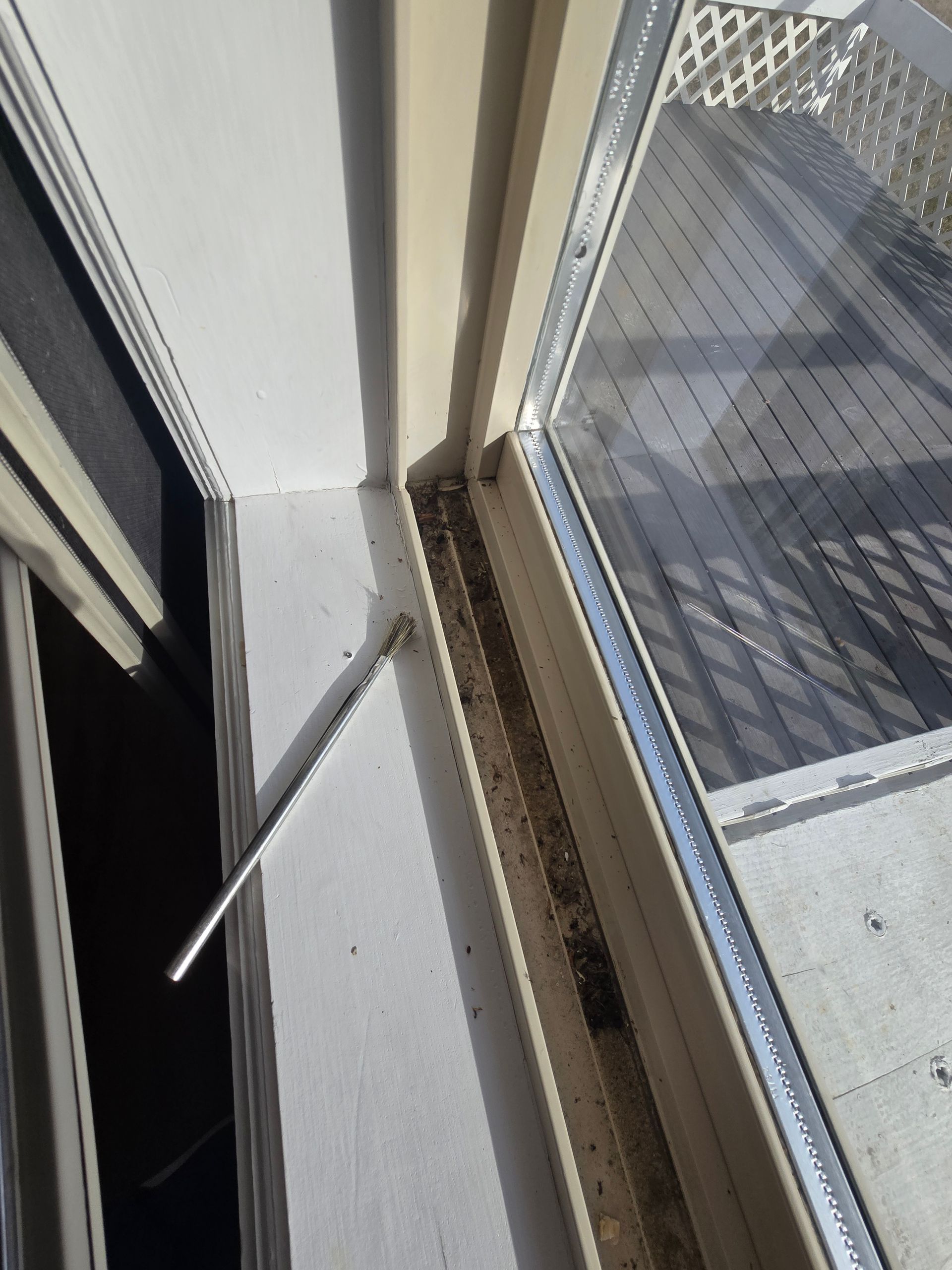 A silver metal window restrictor bar attached to a window frame, with debris visible in the sliding door track.