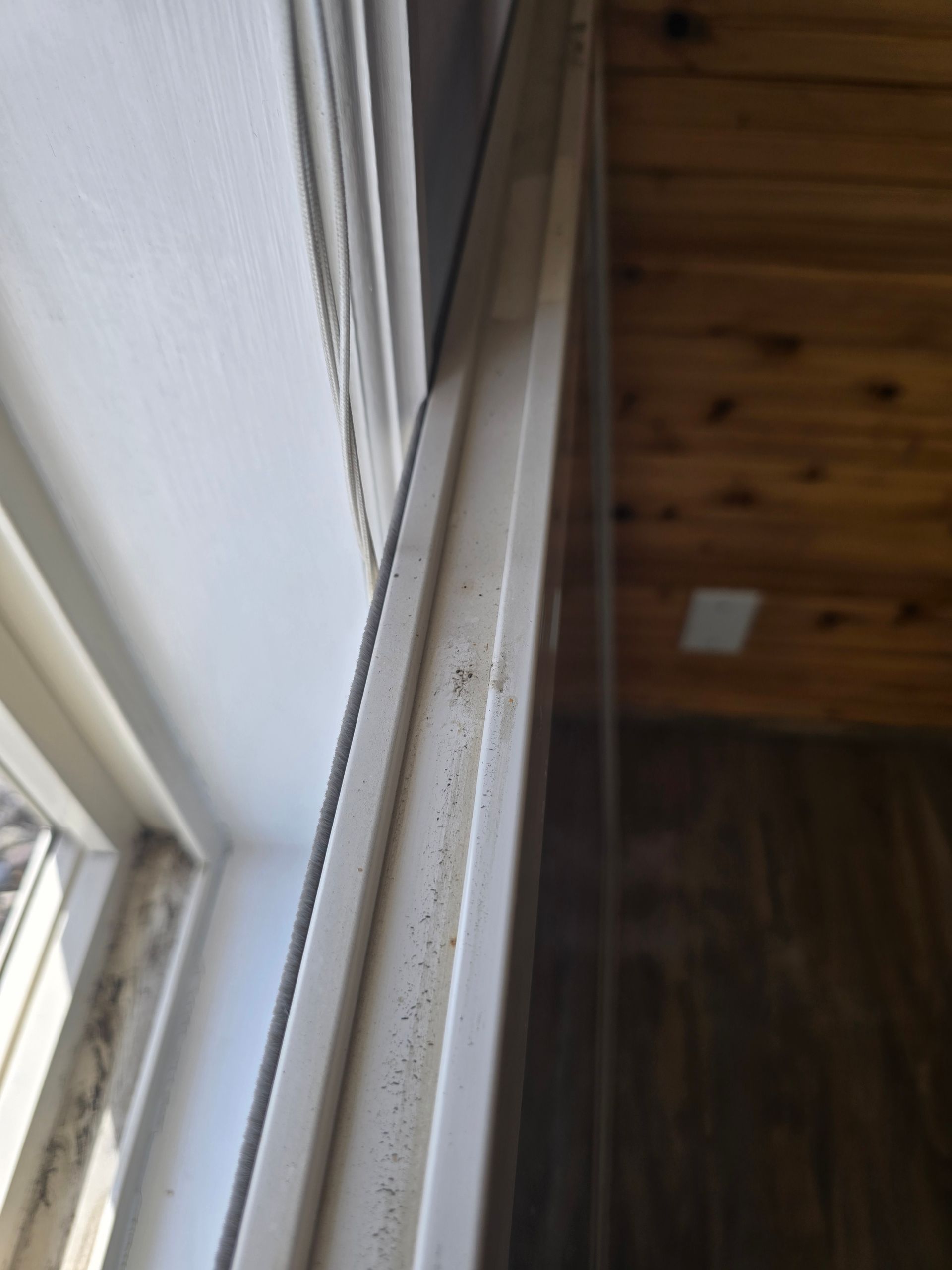 Close-up of a white window frame with a thin track and visible dust or debris along the edge.