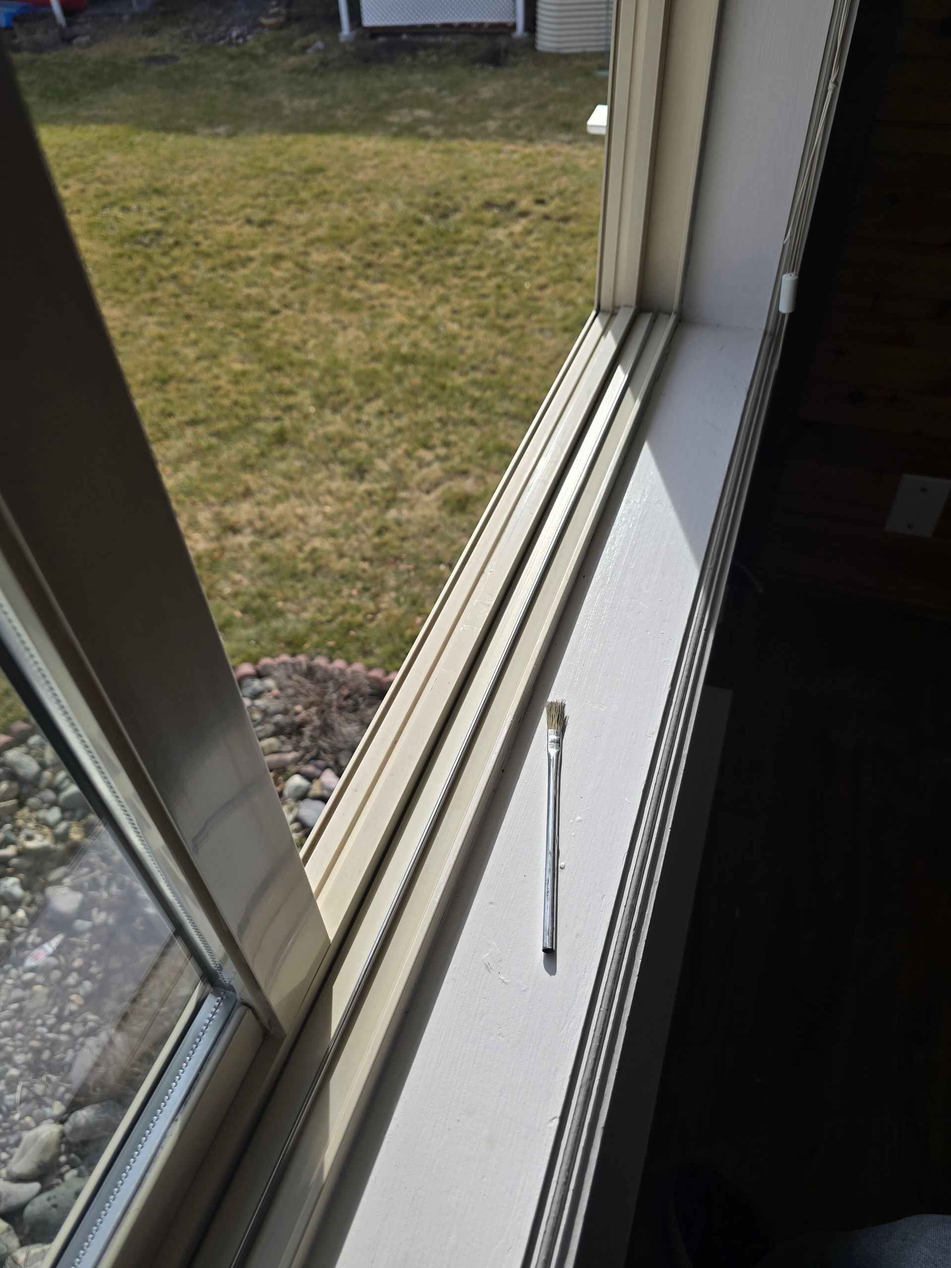 A single toothbrush lying on a white window sill next to a large window overlooking a lawn.