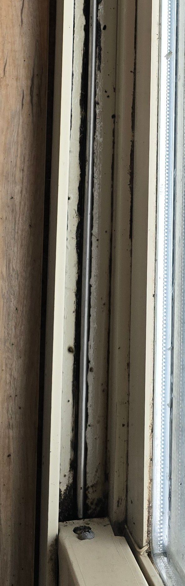 Close-up of a weathered, beige-painted wooden window frame with a vertical gap and cracked paint around the metal track.