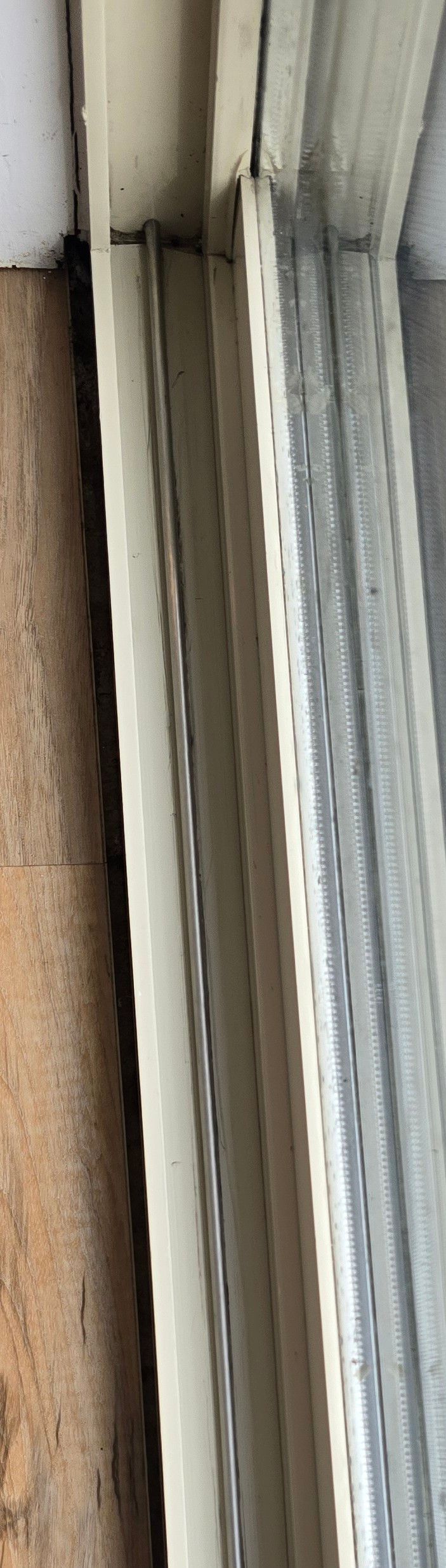 Close-up view of a vertical window frame track made of cream-colored vinyl and gray metal.