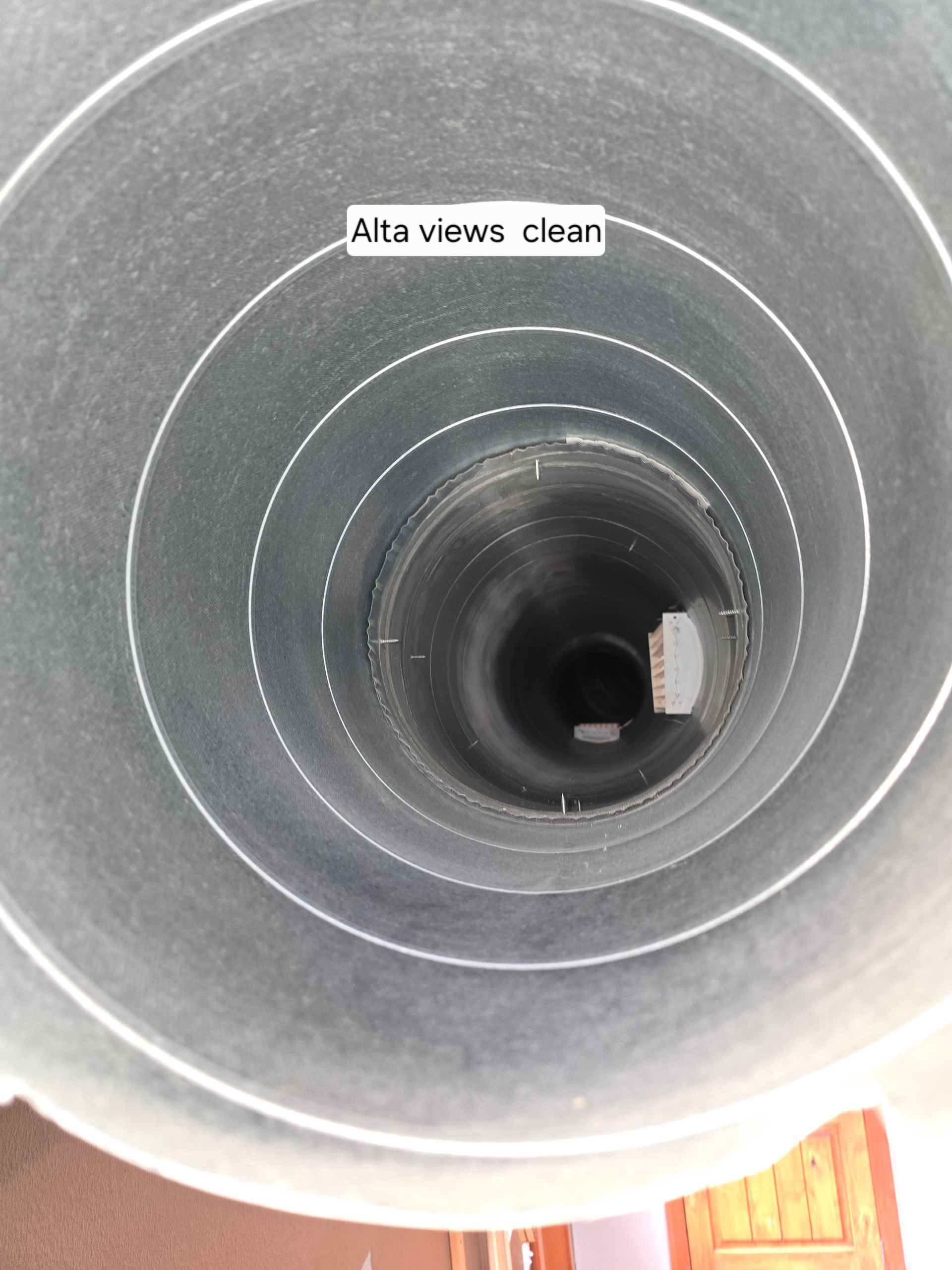 Looking down into a clean, dark gray ventilation duct or chimney showing circular walls and a small opening at the bottom.