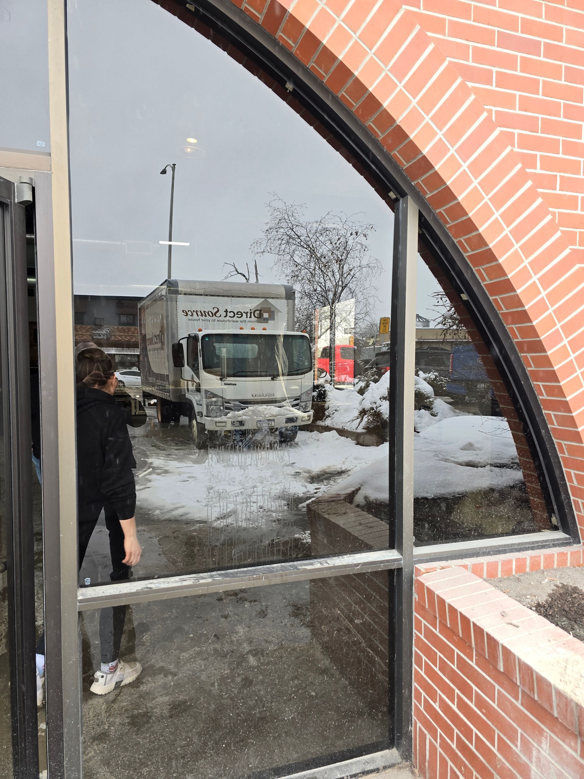 A view through an arched window showing a box truck parked in a snowy parking lot, with a person standing by the door.
