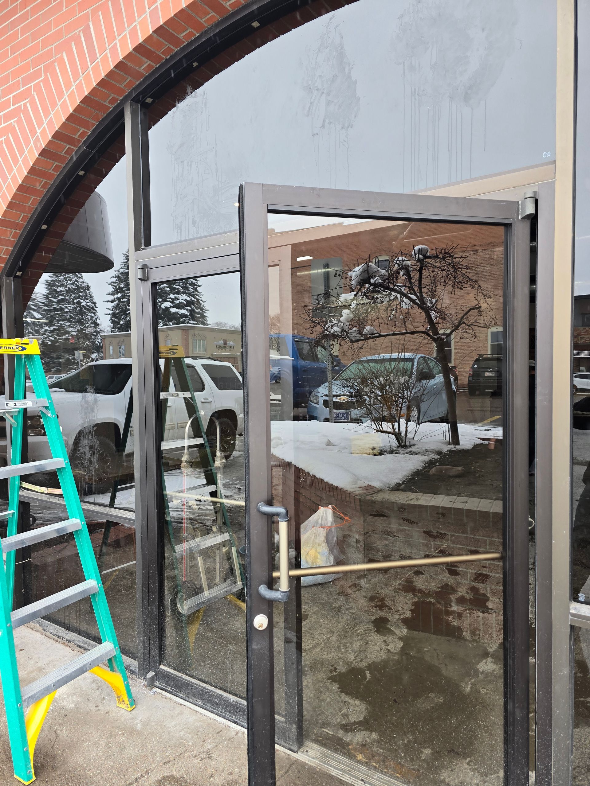 A glass commercial door with a metal frame and handle, with a green stepladder visible to the left.