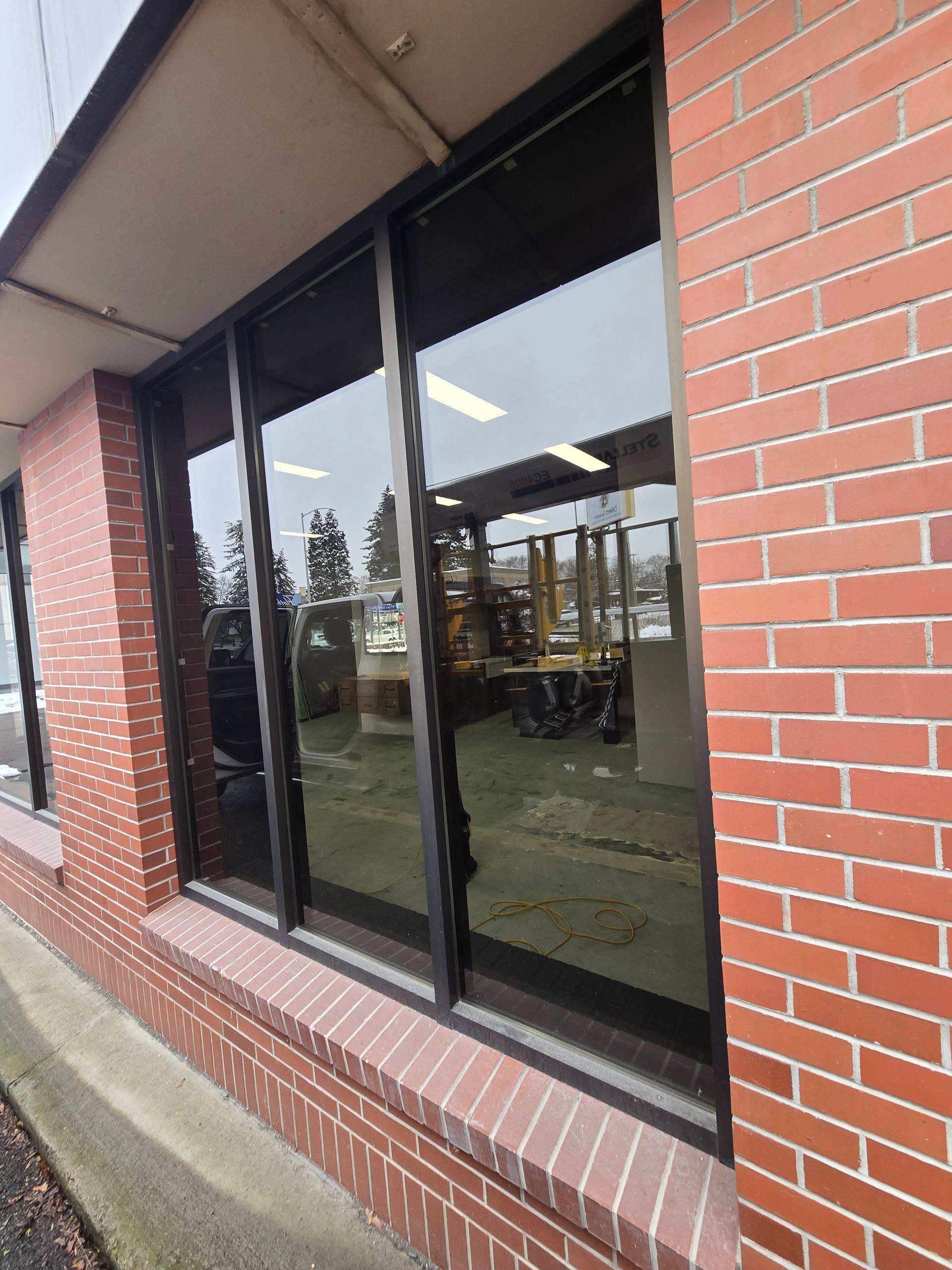 A view through a large window into a brightly lit interior space, framed by a brick exterior wall.