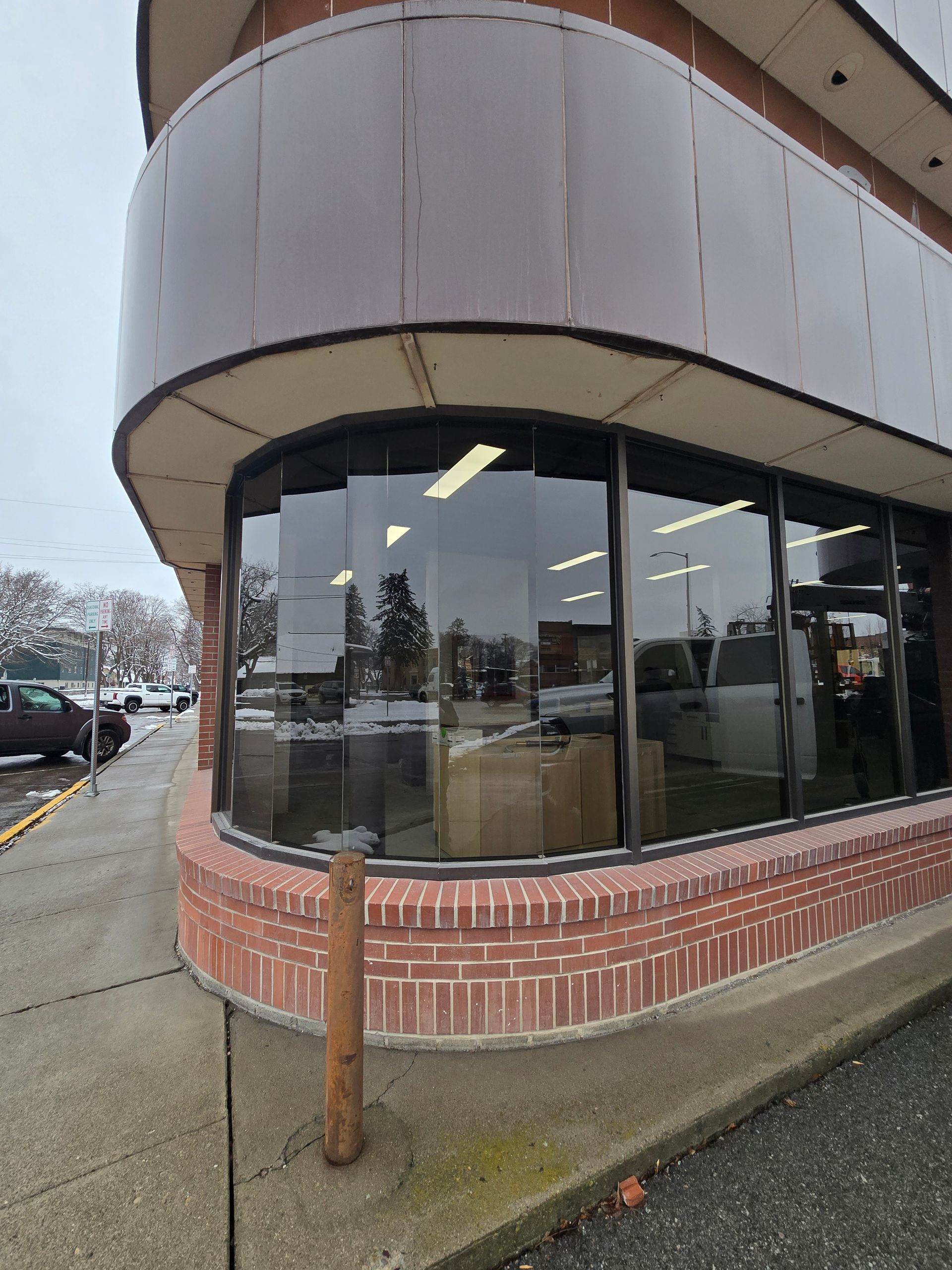 A curved storefront window with a brick base and dark metal trim on an overcast day.