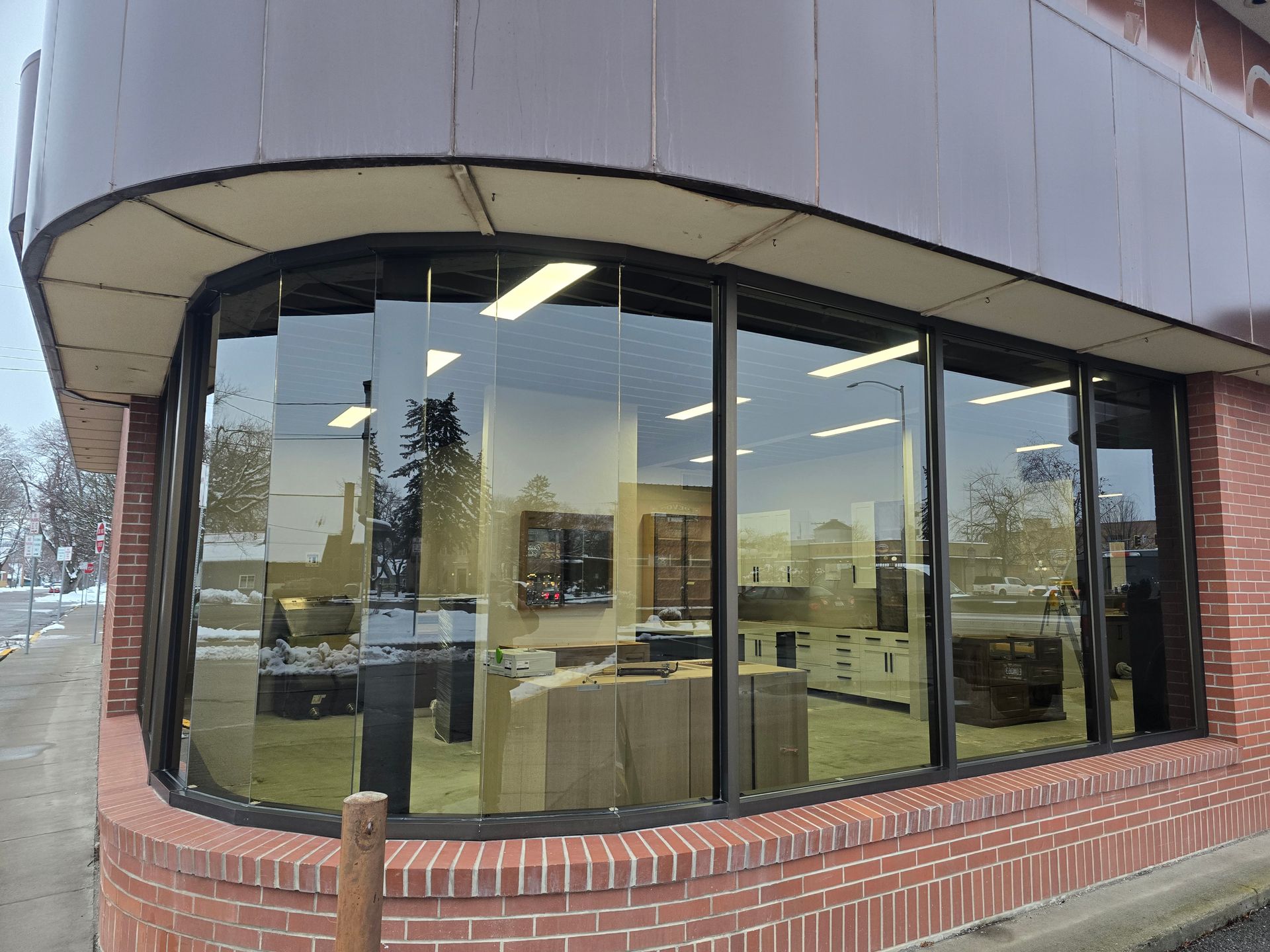 A curved corner window display of a brick building looking into an empty retail office space.