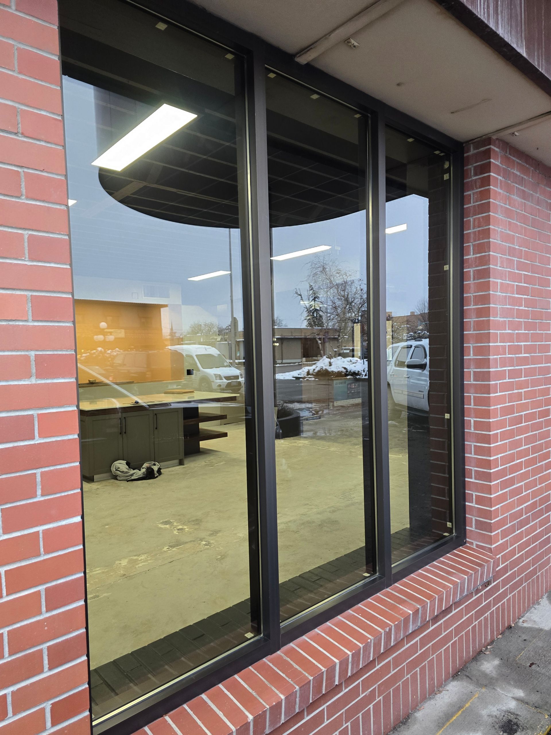 A brick building exterior featuring large, rectangular glass windows that reflect the outdoor environment and interior.