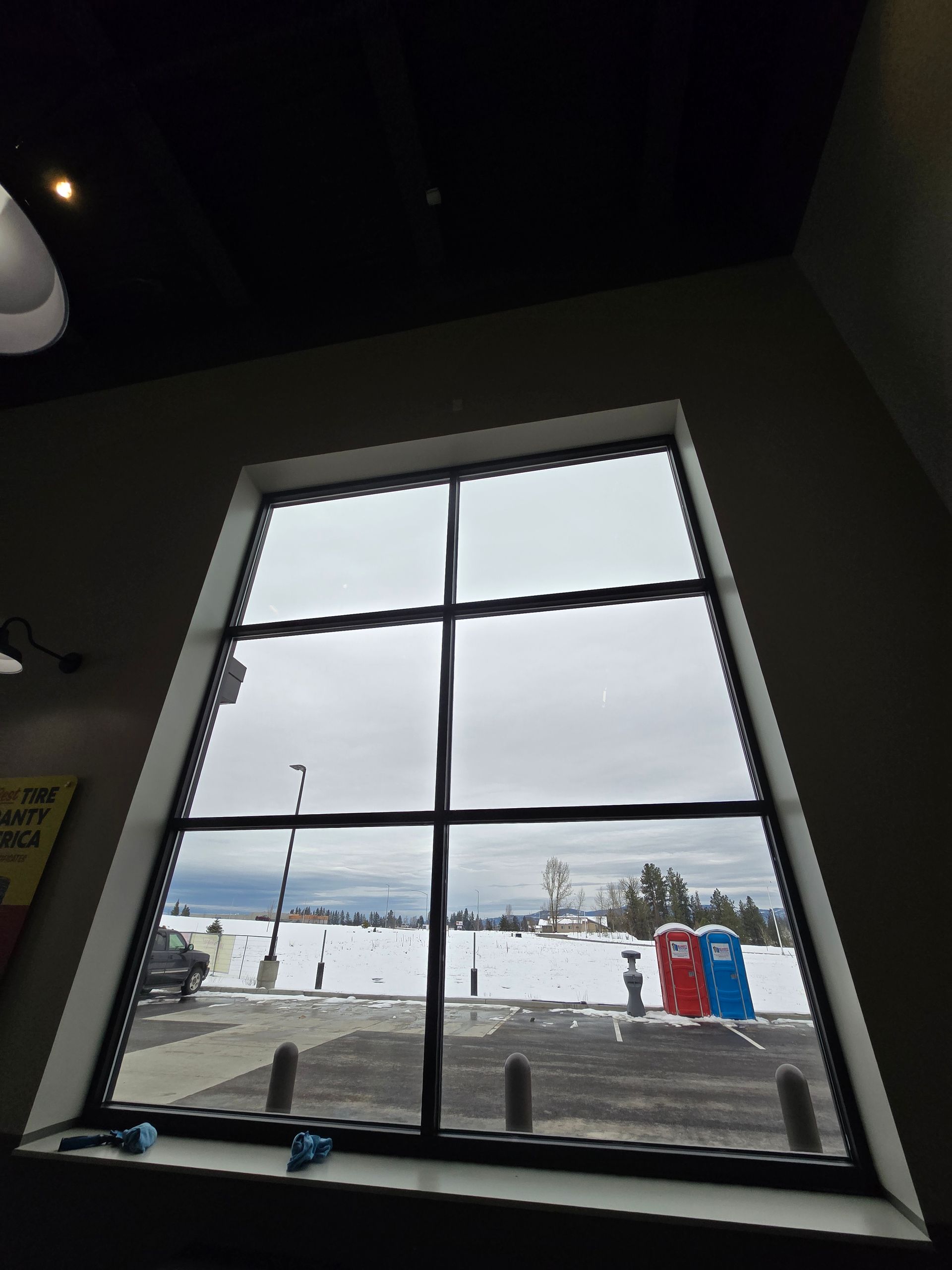 A large window looking out onto a parking lot covered in snow, with two portable toilets visible in the distance.