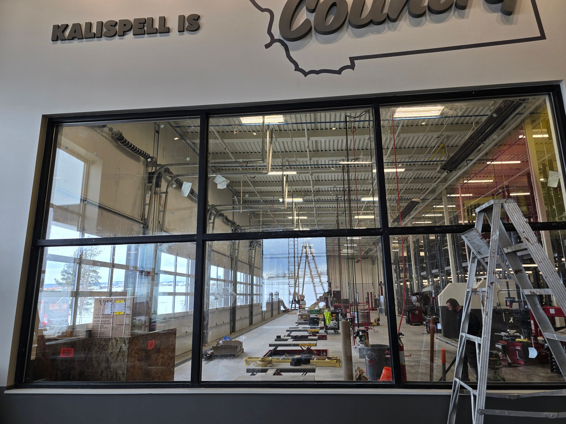 A view through a large window into a brightly lit, industrial warehouse space featuring tools and equipment.