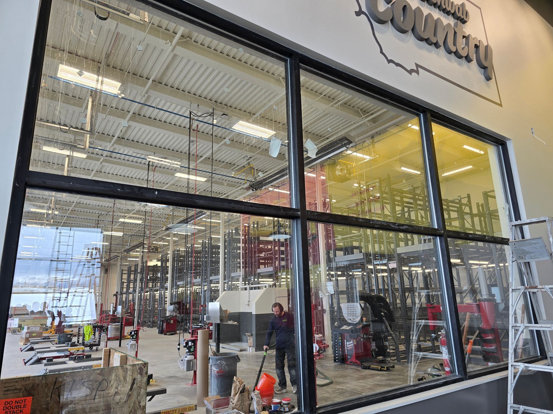 Interior view through a large glass window showing a retail space under construction with tools and supplies.