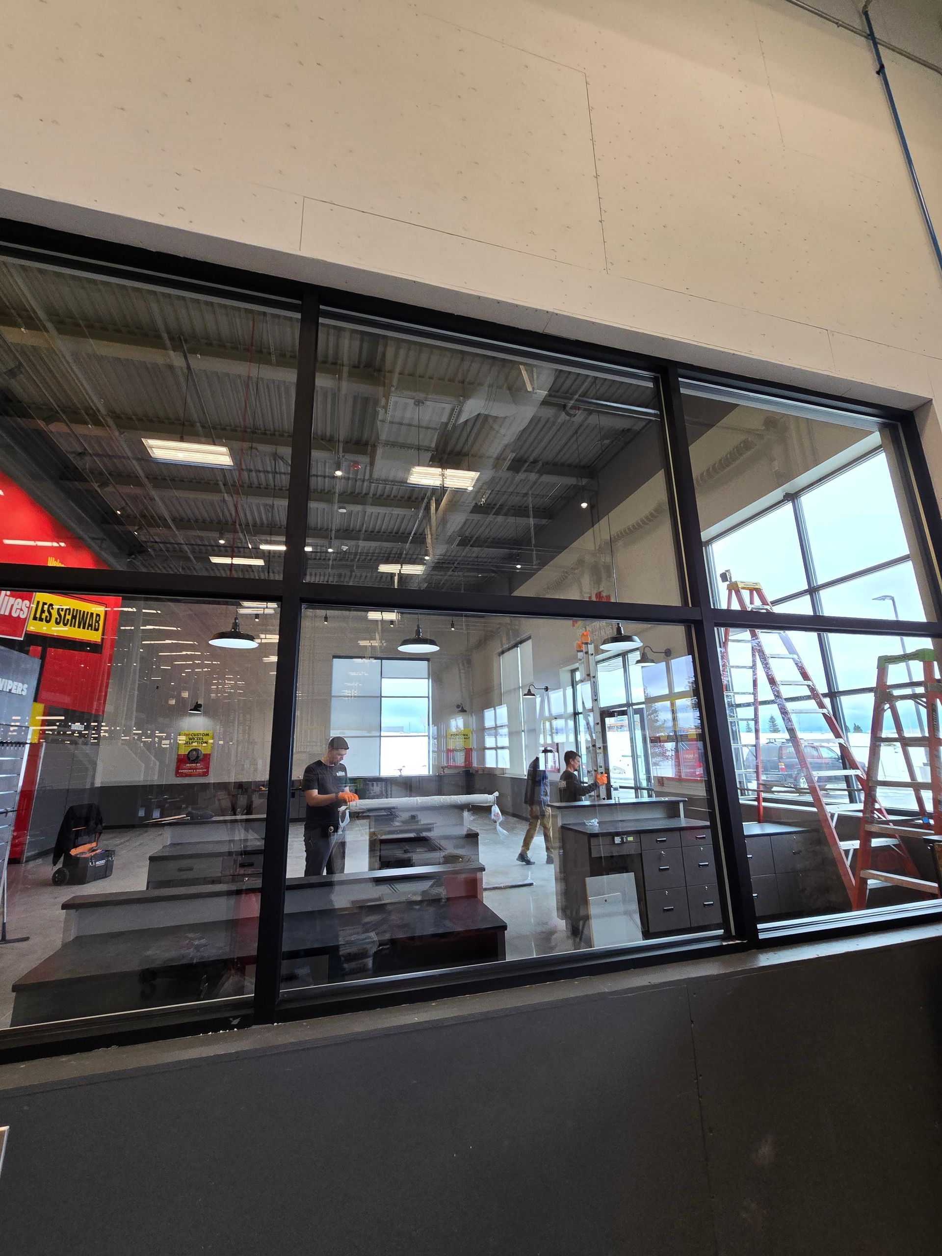Workers install fixtures and equipment inside a retail space viewed through a large window.