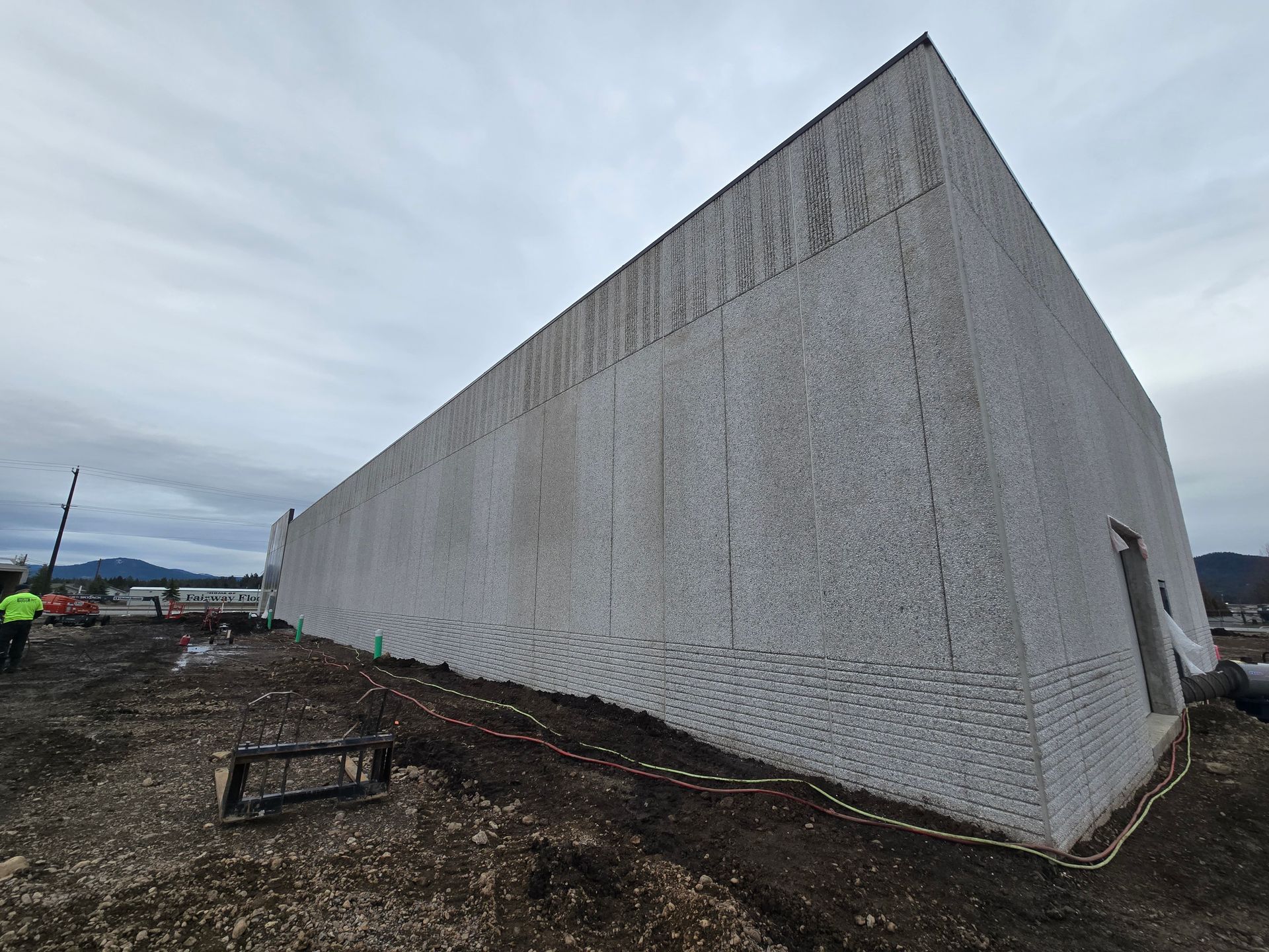 A large, textured light-gray wall under a cloudy sky at a construction site with a worker visible on the left.