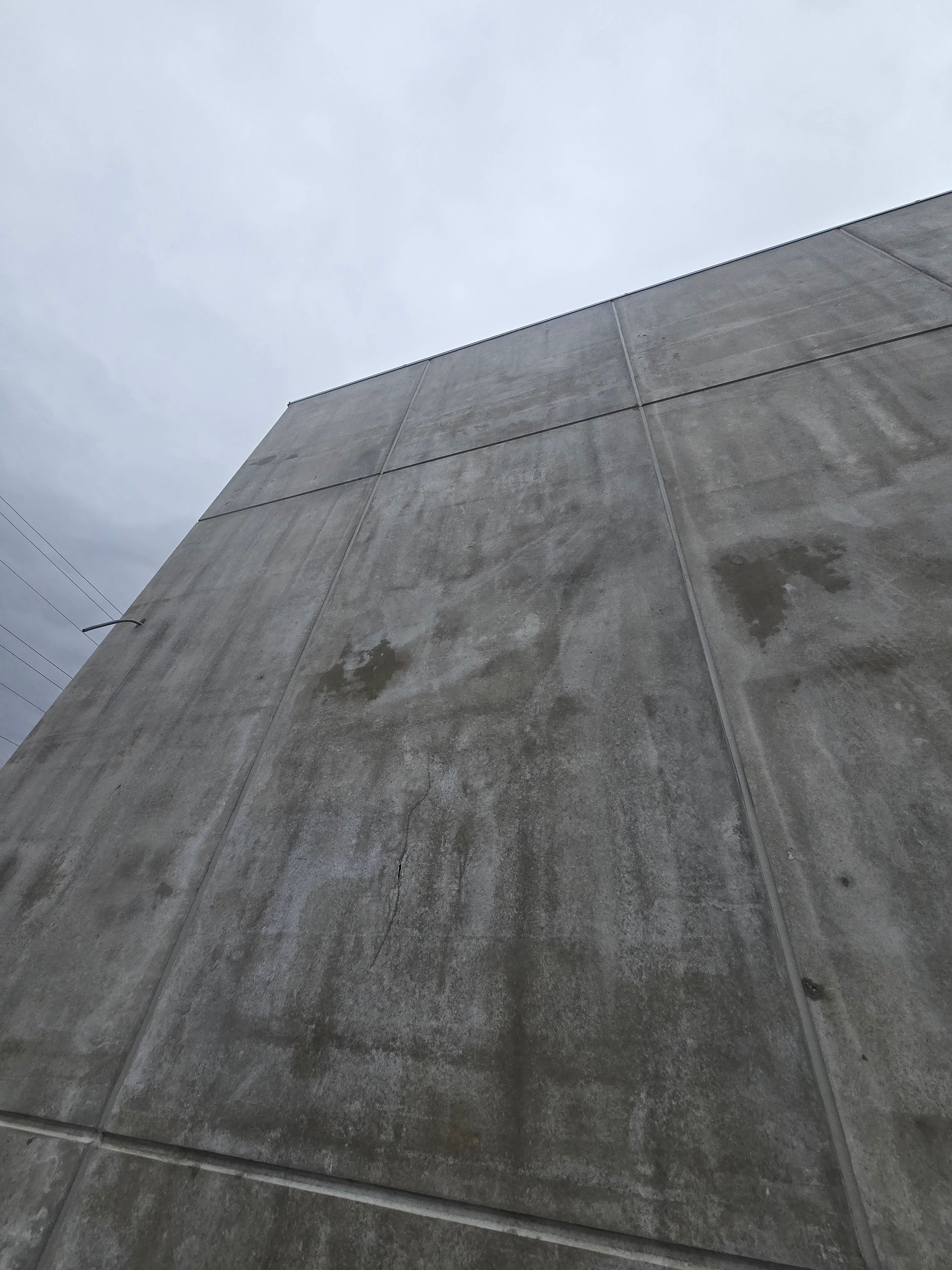 A low-angle view of a gray concrete wall with visible vertical and horizontal panel seams against a cloudy sky.