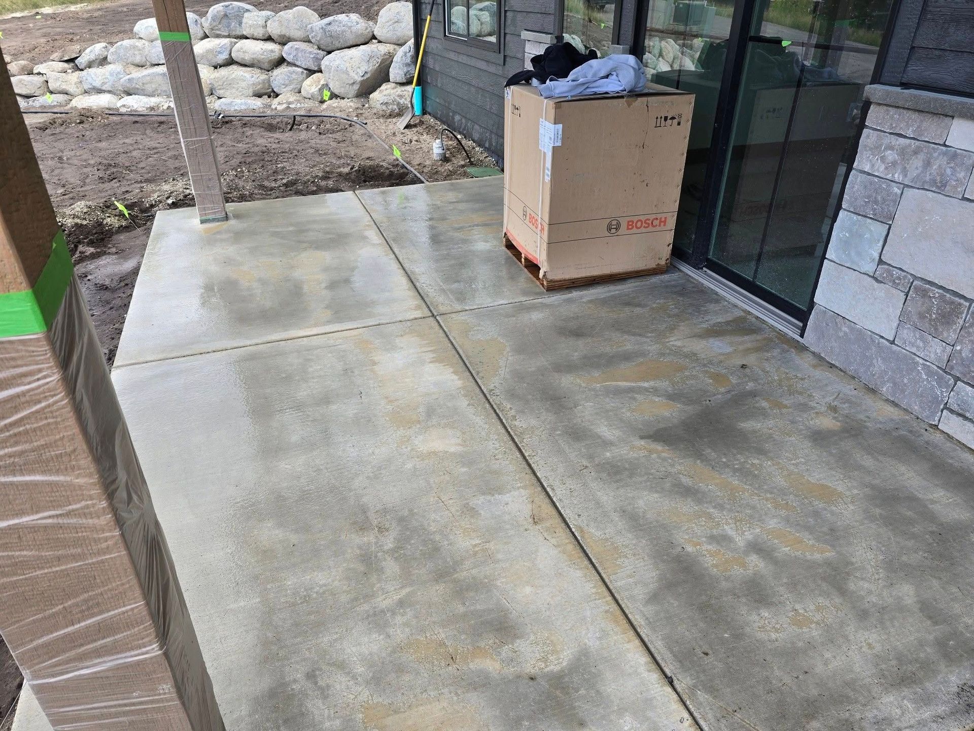 Concrete patio area with a shipping box sitting near a glass door next to a stone-clad wall and a wooden post.