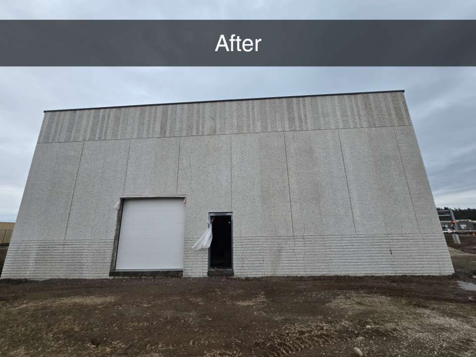 A large, windowless industrial warehouse exterior with gray textured walls, a white roll-up door, and an open side door.
