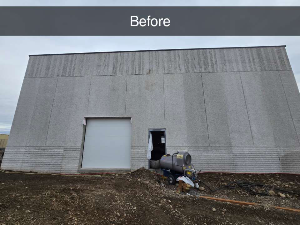 Exterior view of a gray, textured industrial building wall with a closed garage door and an open pedestrian door.