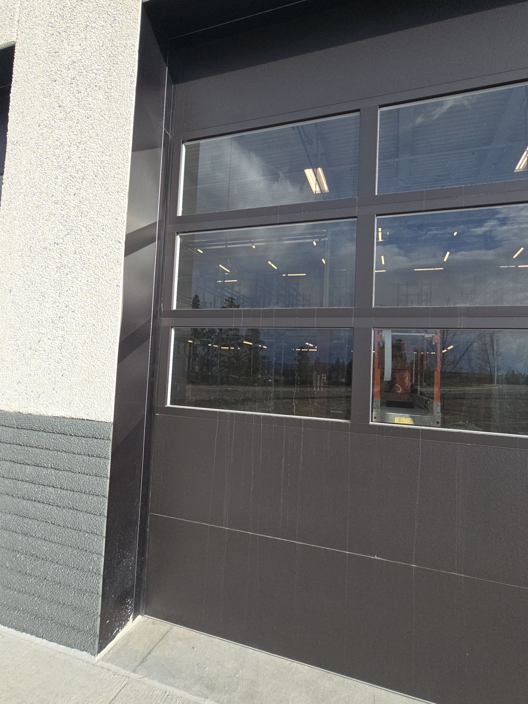 A dark brown industrial sectional garage door with a row of windows set into the wall of a grey building.