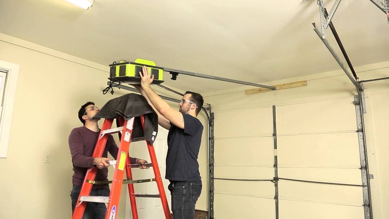 Two men are working on a garage door opener in a garage.