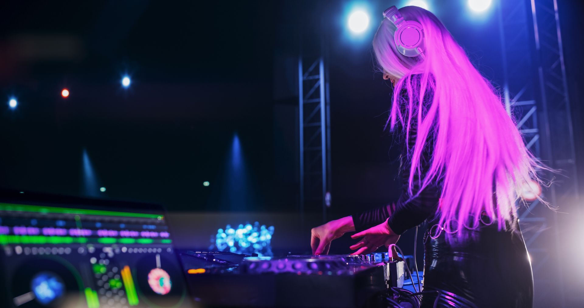 DJ with long white hair mixing music on stage with purple and blue lighting.