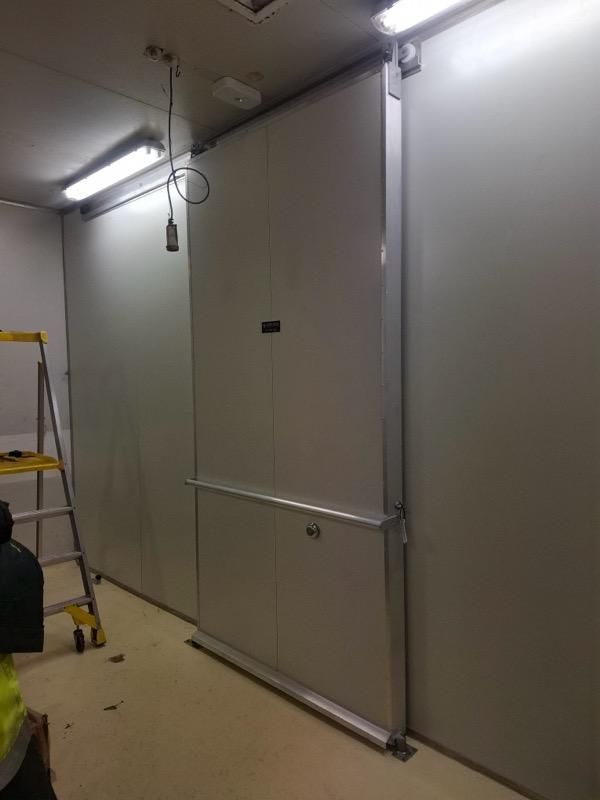 Interior view of a room with white walls and a large, sliding metal door. Fluorescent lights and a ladder are visible — Hutchy's Refrigeration & Electrical in Trinity Park, QLD