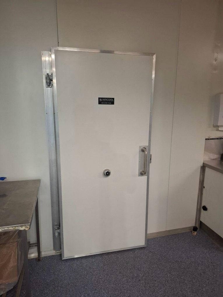 White door with a metallic frame. Small black sign on door. Inside setting — Hutchy's Refrigeration & Electrical in Trinity Park, QLD