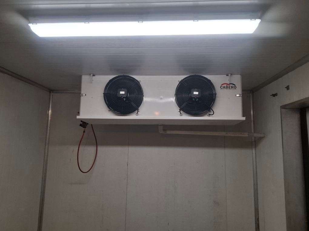 White refrigerator unit with two black fans mounted on a white wall inside a white room, under fluorescent lights — Hutchy's Refrigeration & Electrical in Trinity Park, QLD