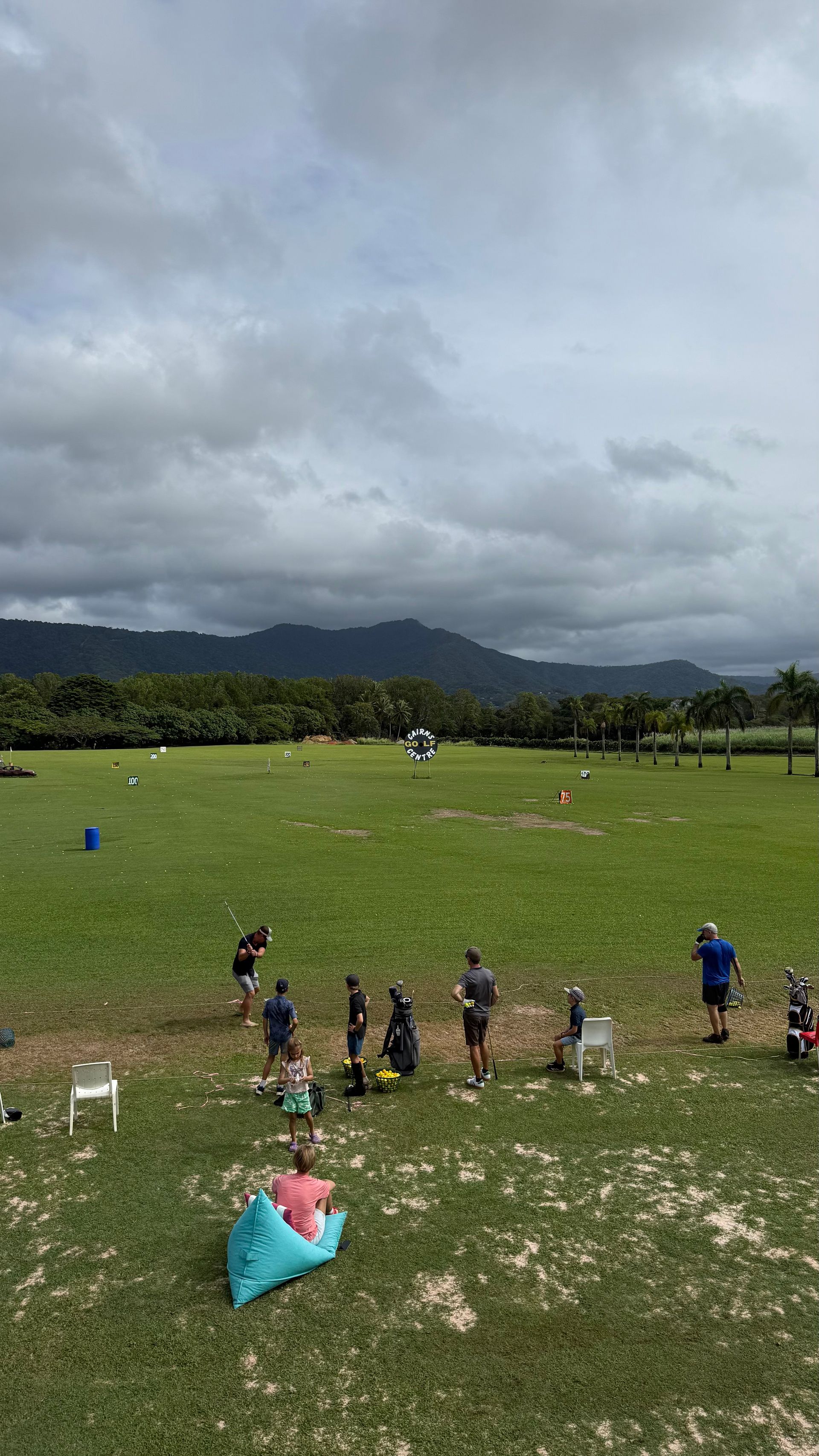A group of people are standing in a grassy field with mountains in the background.