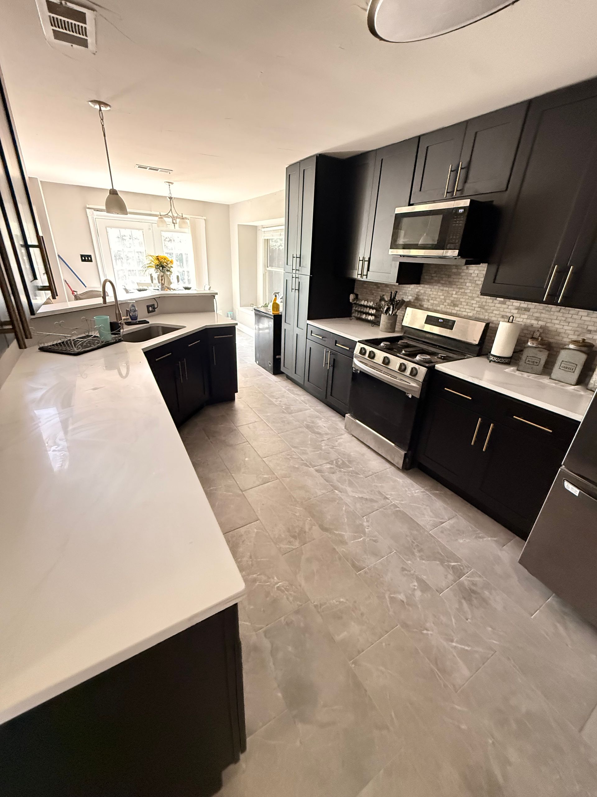 White kitchen with island and white cabinets, black appliances, and grey countertops and backsplash.