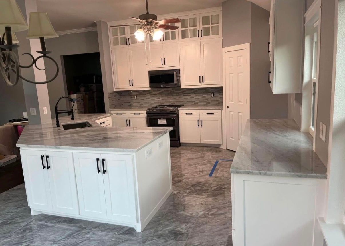 White kitchen with island, cabinets, gray countertops, and black appliances.