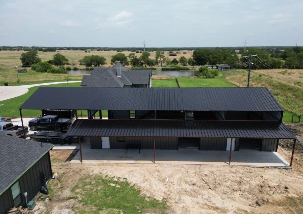 Aerial view of a two-story building with a black metal roof, porch, and concrete foundation in a rural setting.