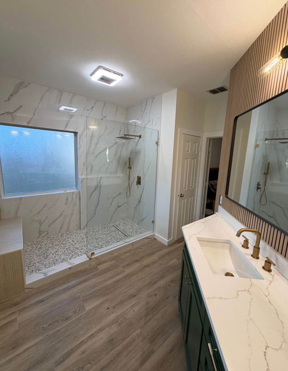 Modern bathroom with a marble-tiled shower, wood floors, and a dark green vanity.