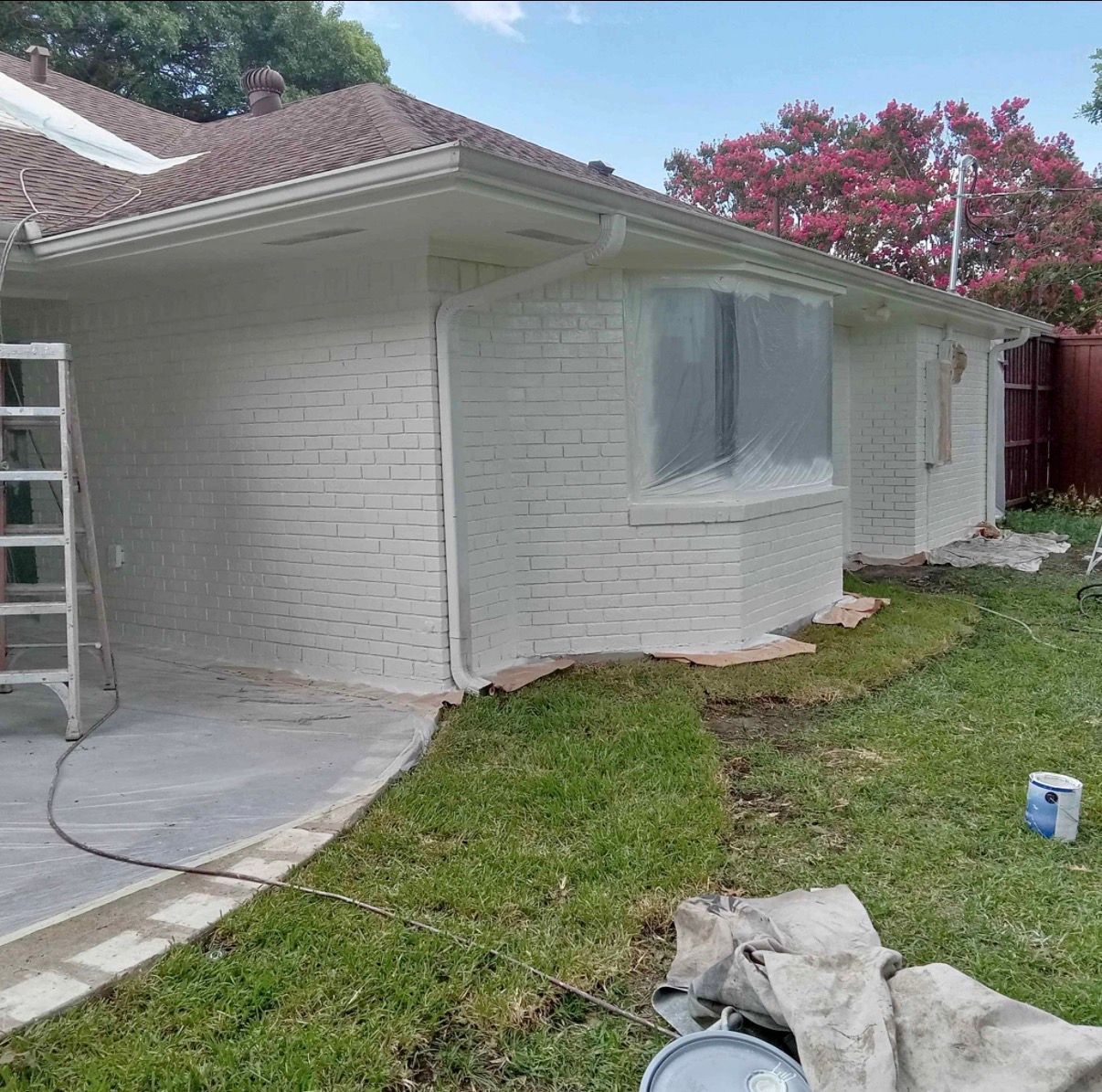 House exterior being painted white, with a ladder, covered windows, and green grass.