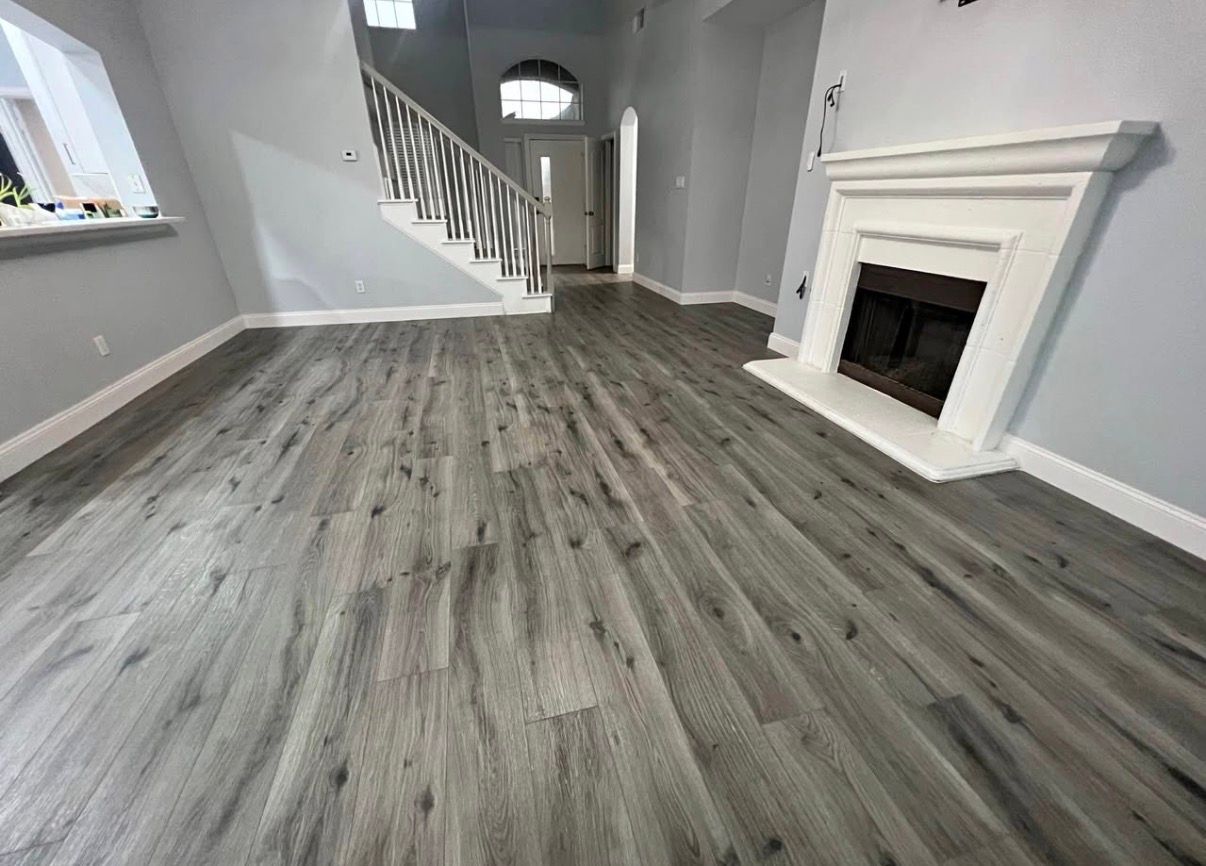 Living room with gray wood-look flooring, fireplace, and stairs leading upstairs.