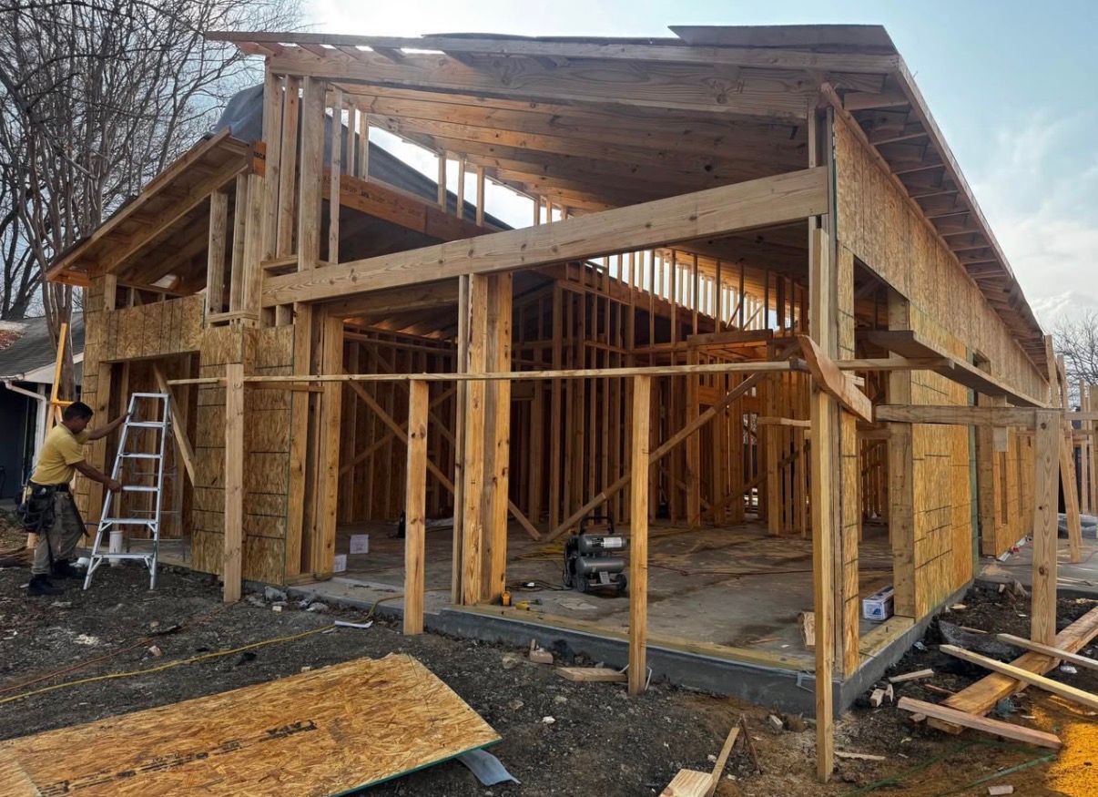 Framing of a building under construction; worker on a ladder, wooden beams and walls visible.