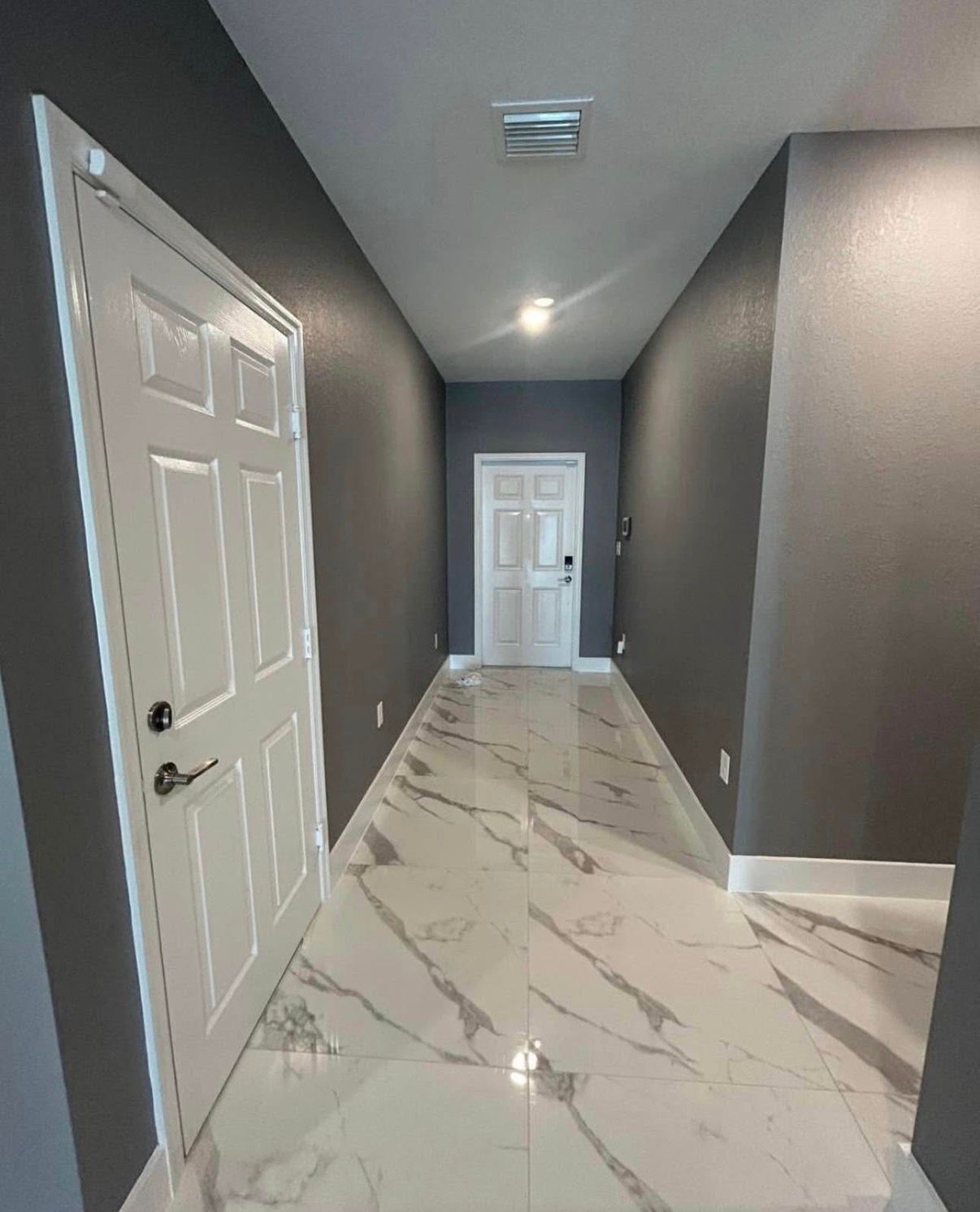 Long hallway with white marble floor and dark gray walls, white doors at ends.