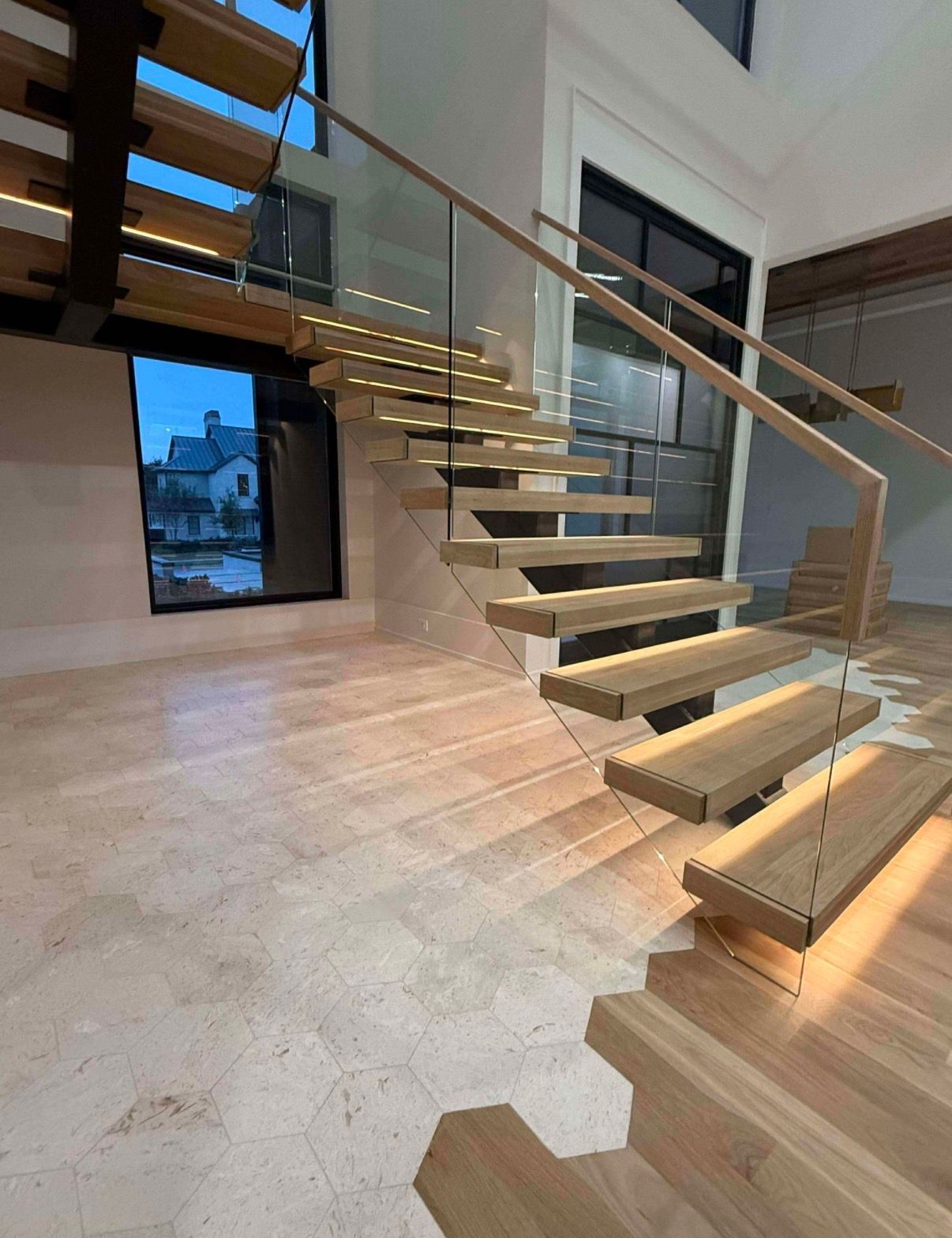 Wooden floating staircase with glass railing, lit steps, in a modern, well-lit interior.